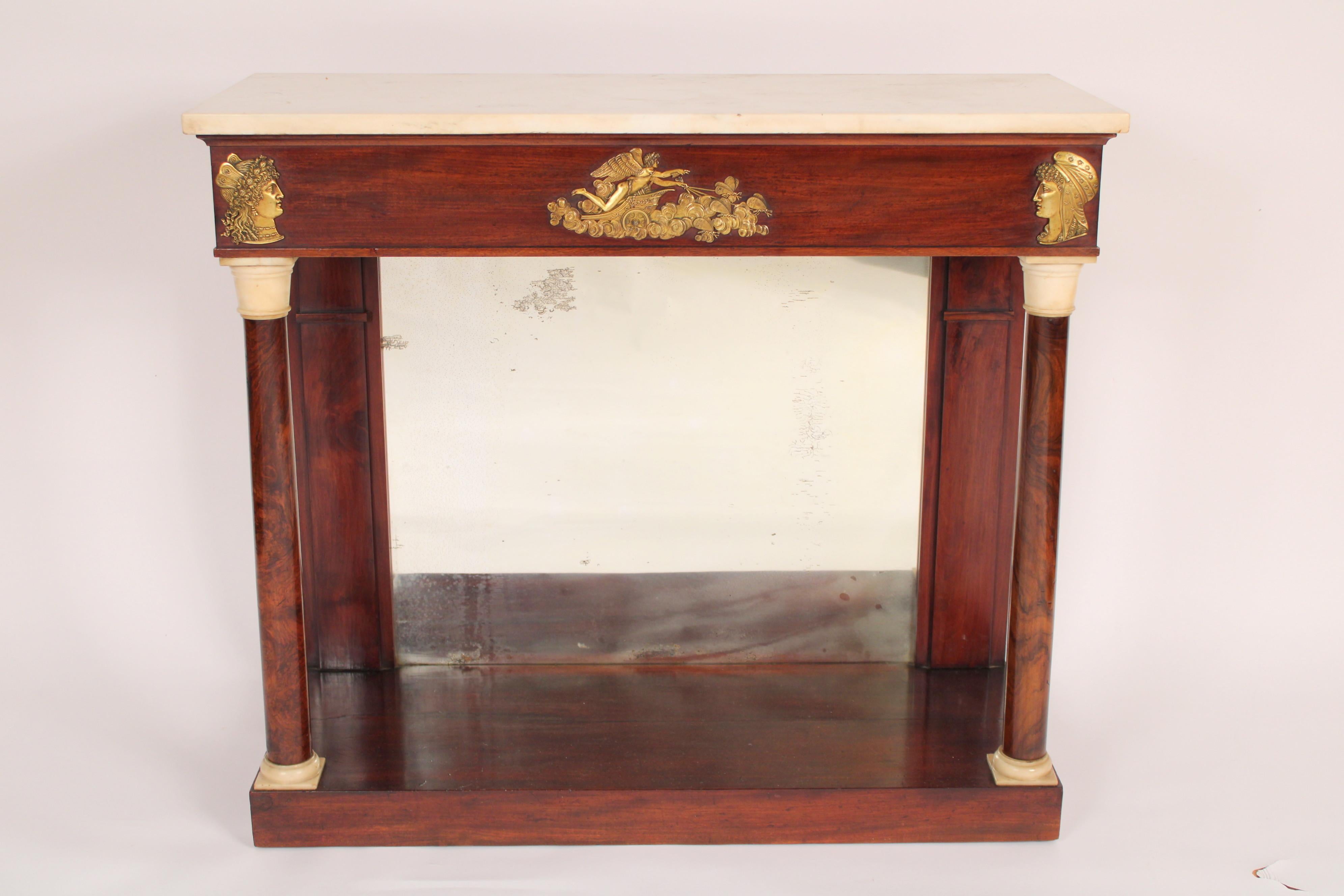 Antique Empire style mahogany console table with marble top, 19th century. With a rectangular Carrera marble top, a frieze with gilt bronze male and female faces in profile on either side of a gilt bronze plaque of an angel riding a chariot in the