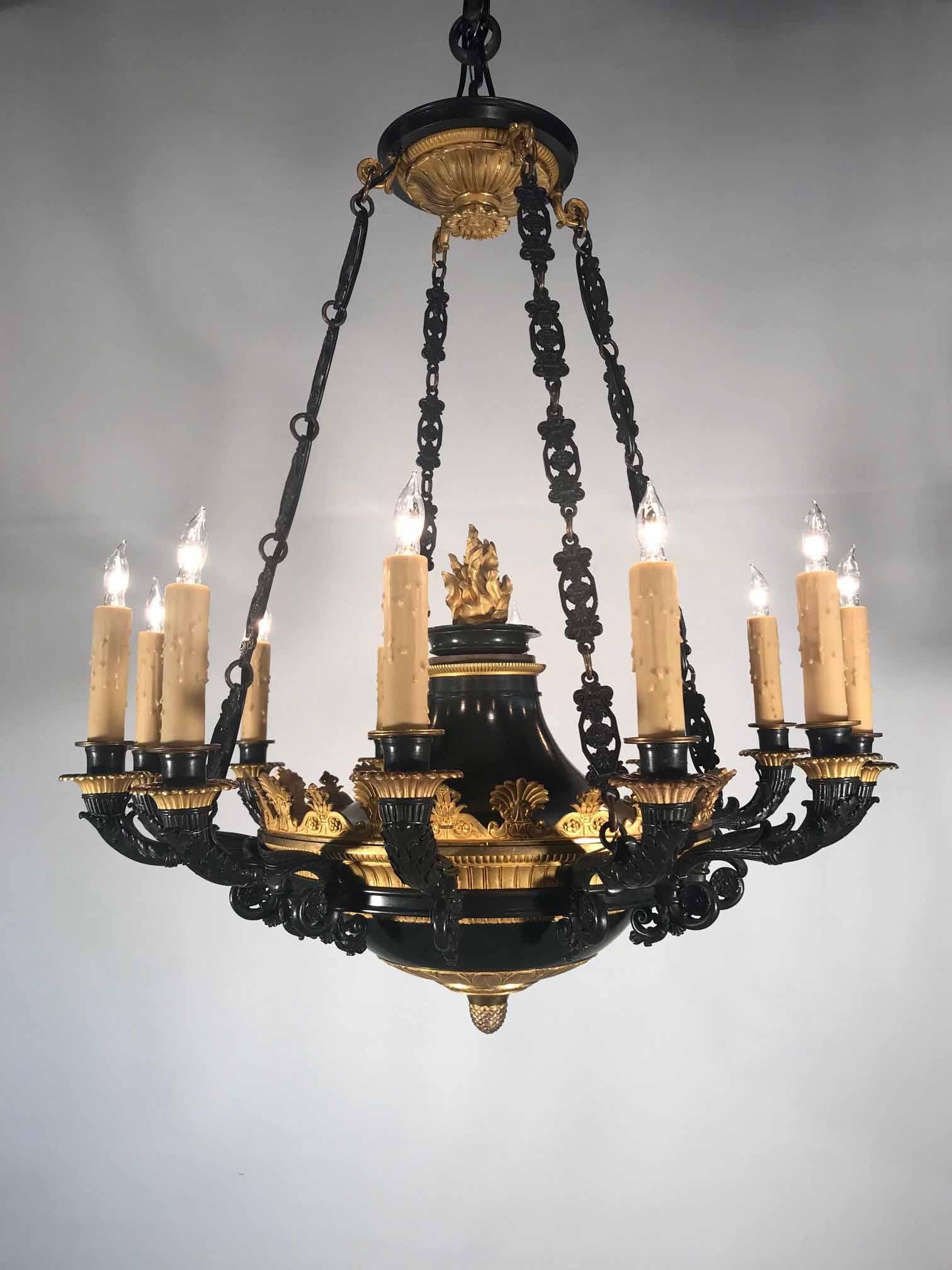 This chandelier combines an understated crisply cast dark bronze body with wonderful quality two-tone gilding. Of classical inspiration, the theme is leafy, repeating borders of anthemions and palmettes: with the canopy, flambeau central flame and