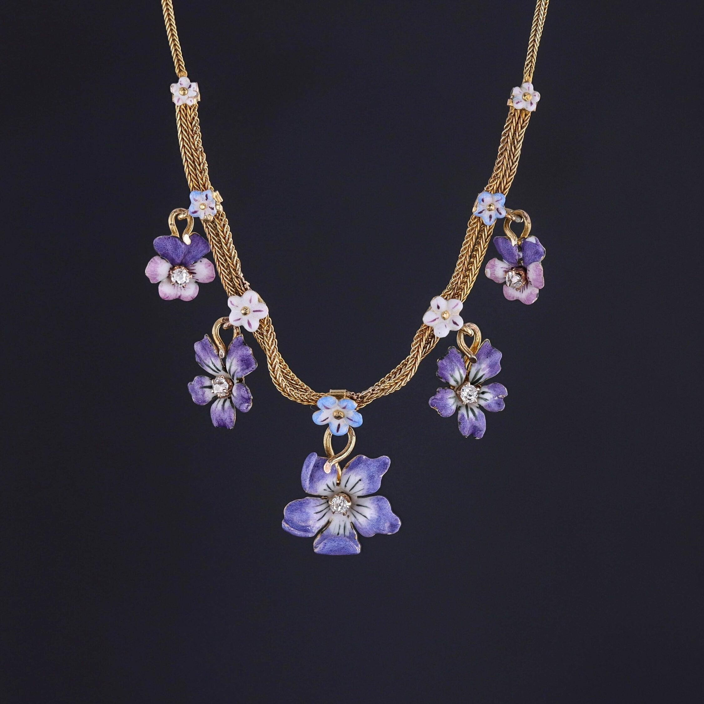 This antique necklace (circa 1910) features an array of enamel forget-me-nots, violets, and pansies set in 14k gold. Each of the flower dangles is accented with a diamond. 

The necklace measures 15 inches long, and it is in very good condition with