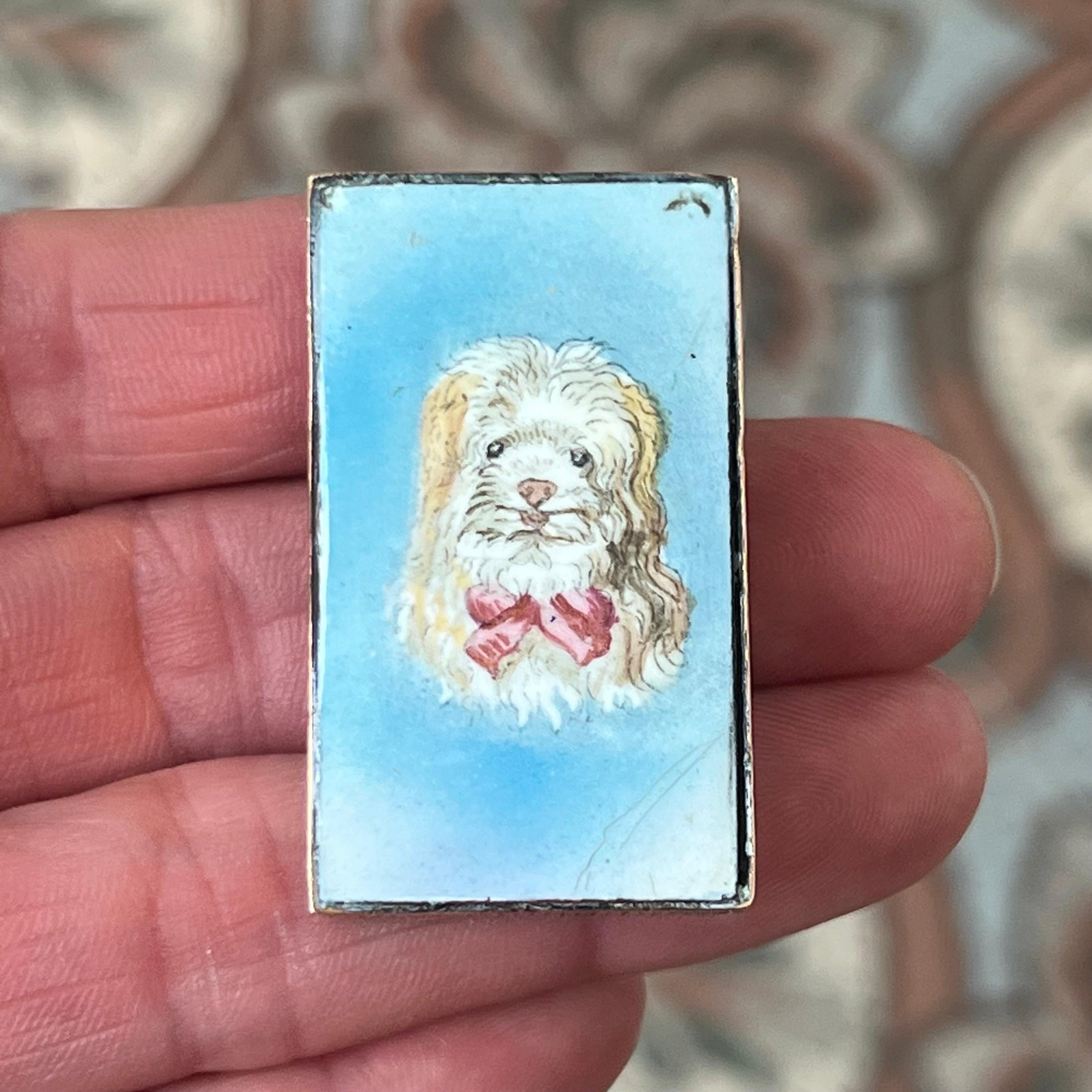 Ein bezauberndes antikes Vesta-Etui (streichholzsicher) mit einem wunderschön handgemalten Emaille-Porträt eines langhaarigen Hundes mit roter Schleife vor einem sanften blauen Hintergrund. Dieses reizvolle Stück wurde um 1900 gefertigt und zeigt