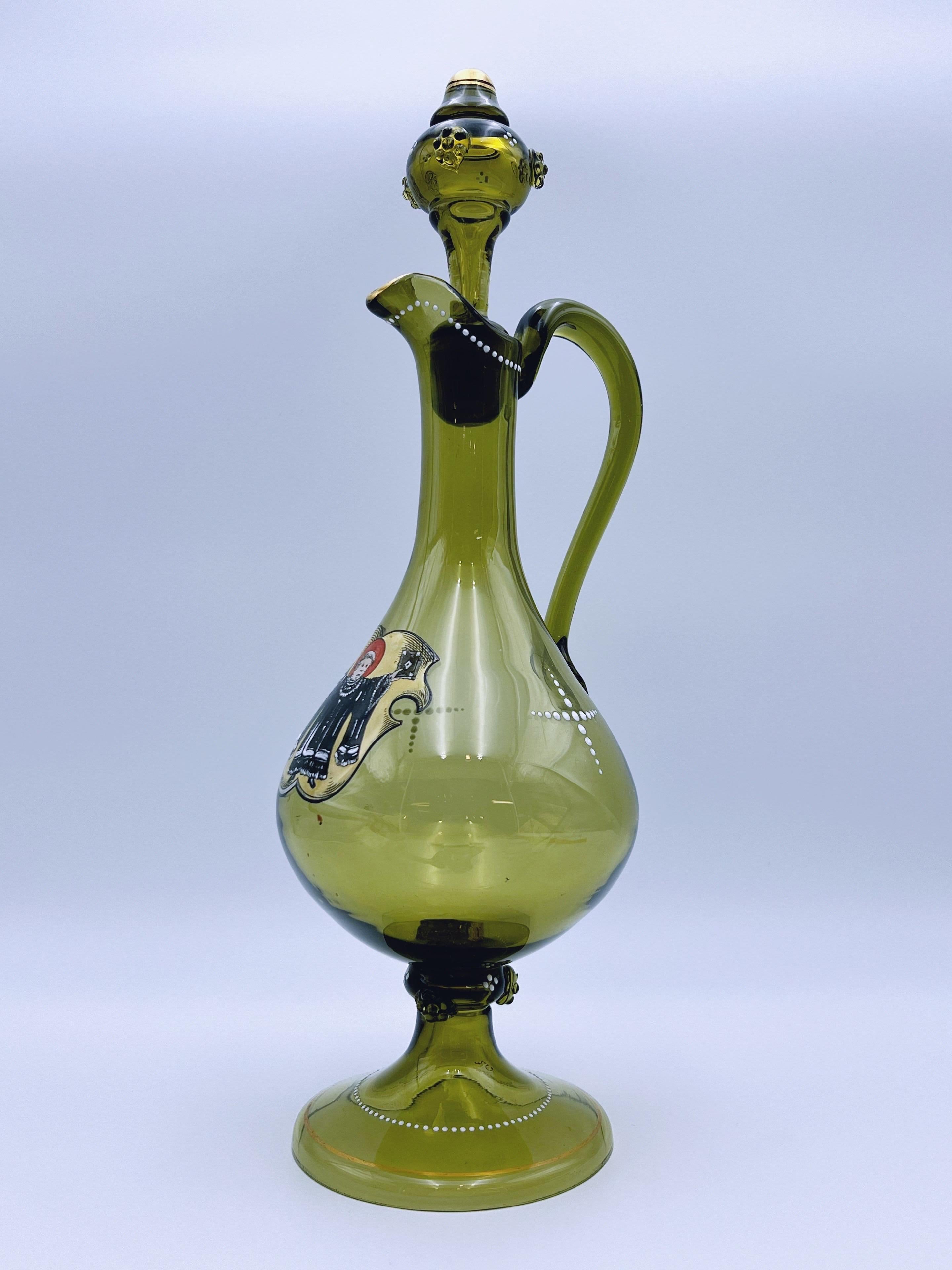 Stunning Antique Brownish-Green / Olive Green Tinted Glass Jug, Gilt and Enamelled in Red, Black, Gold, and White, Circa Late 19th Century.

This exquisite piece features a hand-painted enamel motif at the center, adorned with delicate white enamel