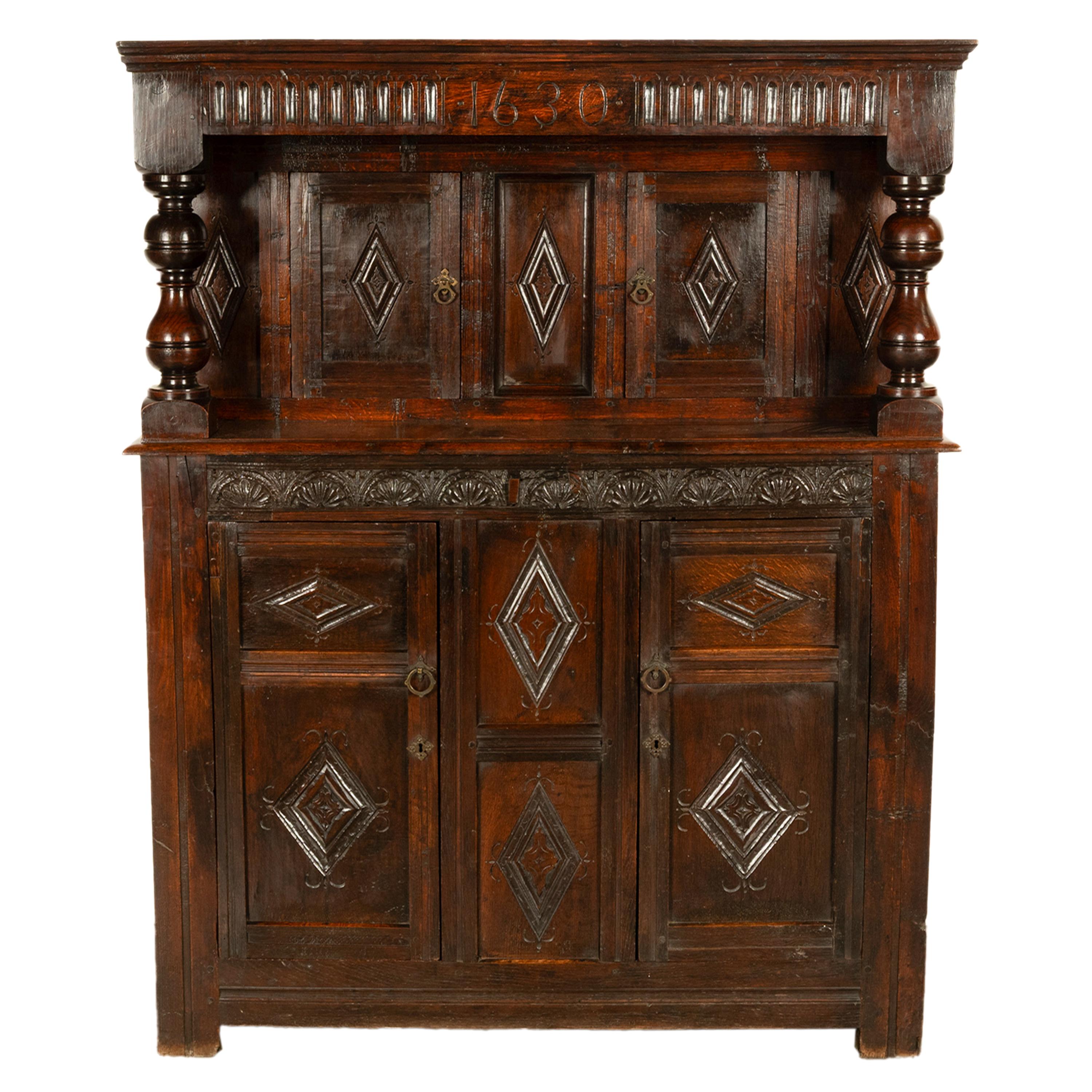 An important antique English Jacobean carved oak court cupboard, from the reign of King Charles I, dated 1630.
The rectangular overhanging top with a carved arcaded frieze, to the center the cabinet has the carved date of 1630, the top supported by