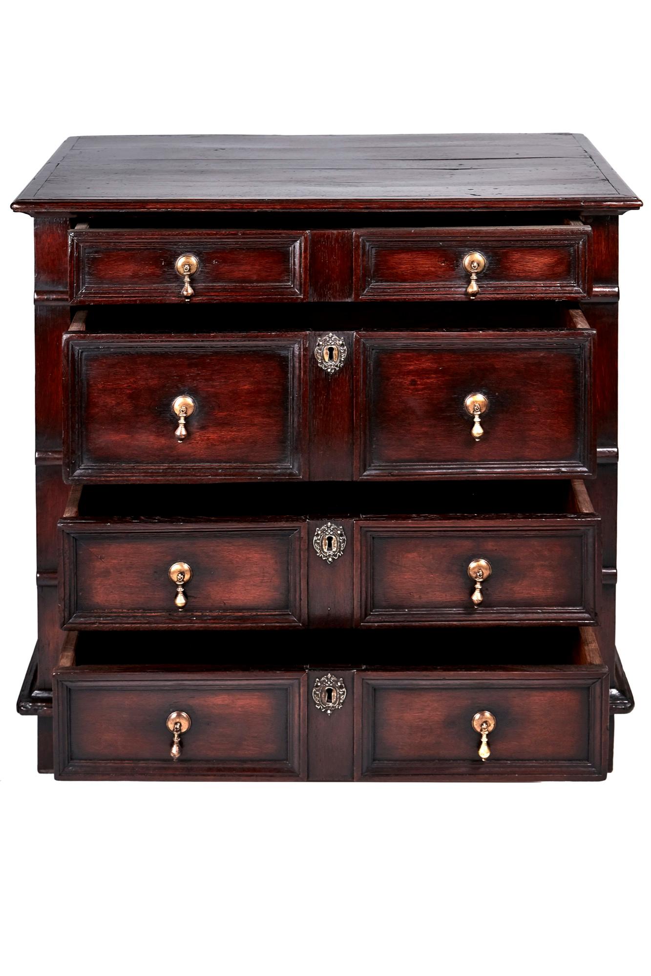 Antique English 17th century William and Mary Jacobean oak chest of drawers having a beautiful top and paneled sides. The four long drawers have moulded fronts and very pretty original brass teardrop handles. The original three ornate brass locks