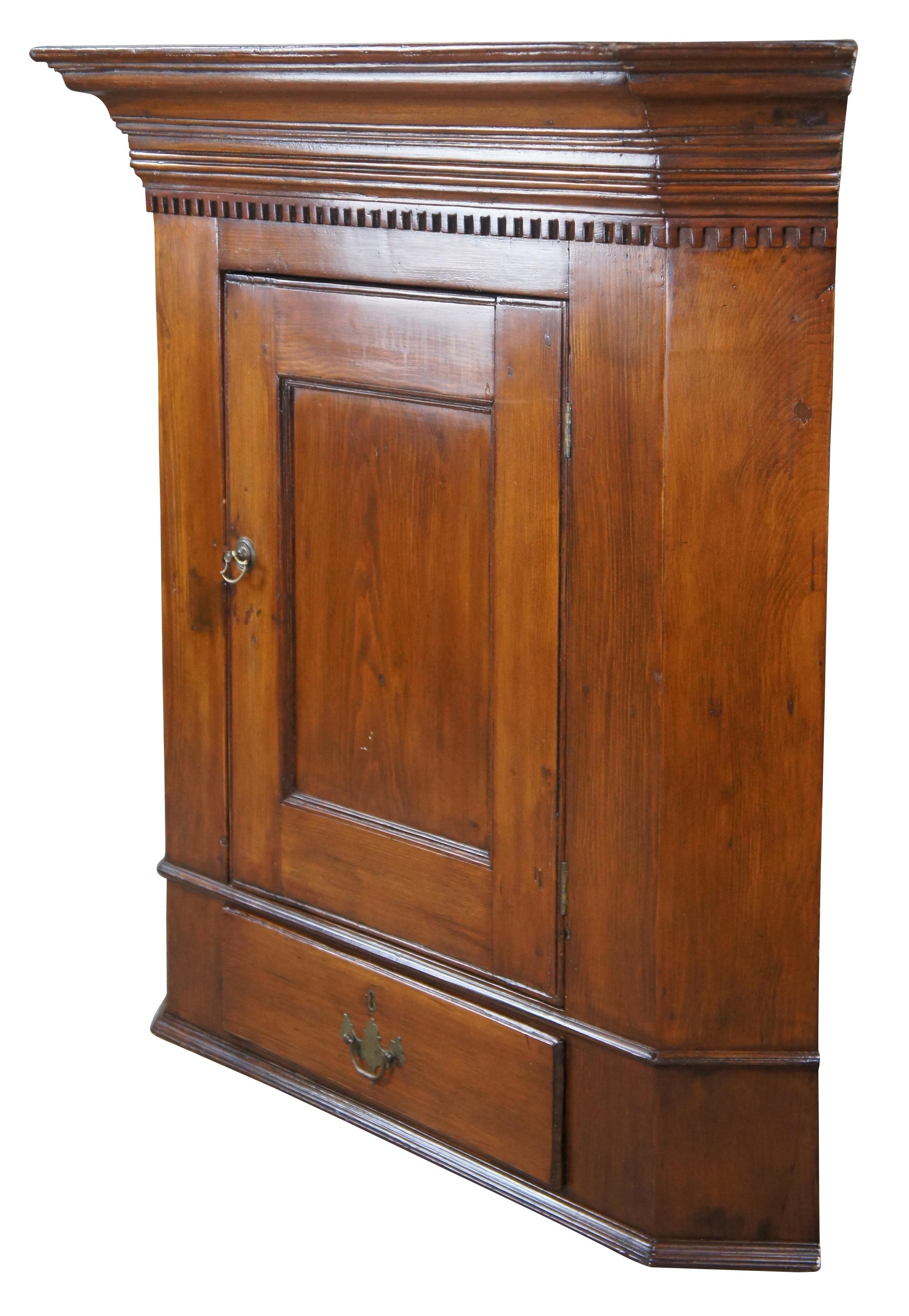 Antique Georgian corner cabinet.  Made of pine featuring ornate dentil crown molding with upper cabinet and lower hand dovetailed drawer.  Fitted with modern brass hardware from Ball & Ball of Whitford.

38