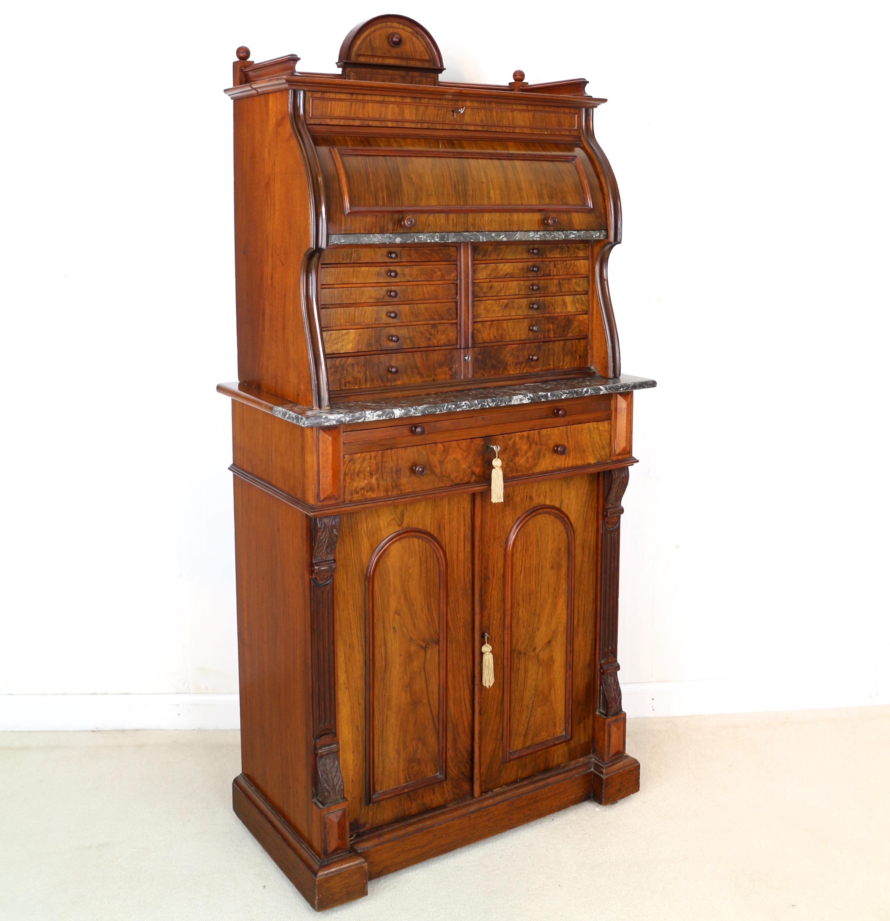 A super Victorian figured walnut dentist’s cabinet attributed to ‘The Dental Manufacturing Co. Ltd’ . The top with an arched back and three quarter moulded gallery with turned finials above a lockable revolving cylinder door which opens to reveal