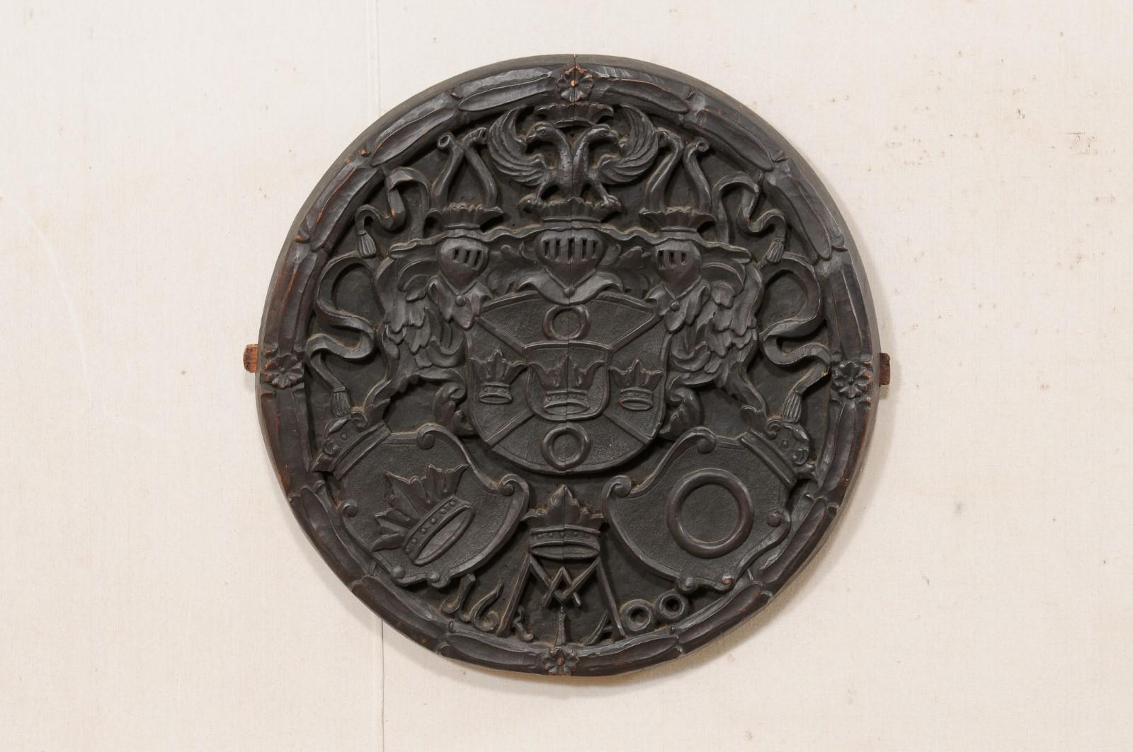 An English carved wood plaque from the later 19th century. This antique wall decoration from England, which is circular-shaped and 2 feet in diameter, has been hand-carved with a shield of crowns at center with three knights above, and pair of