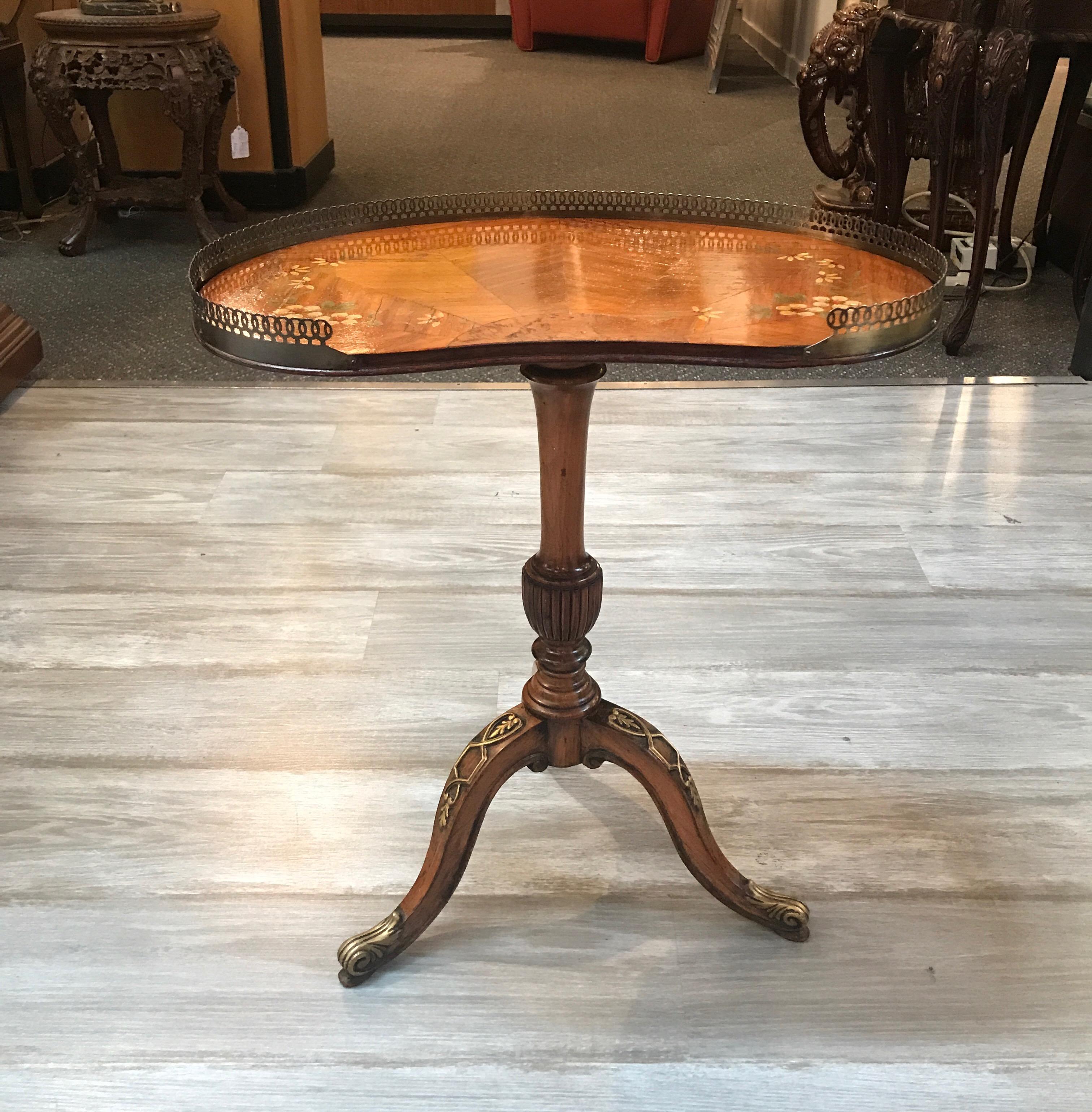 Graceful diminutive English Adam style drinks table with reticulated brass gallery edge. The kidney shaped top in a mellow satinwood with hand painted decoration around the edge. The hand carved base with center urn form column on three gracefully