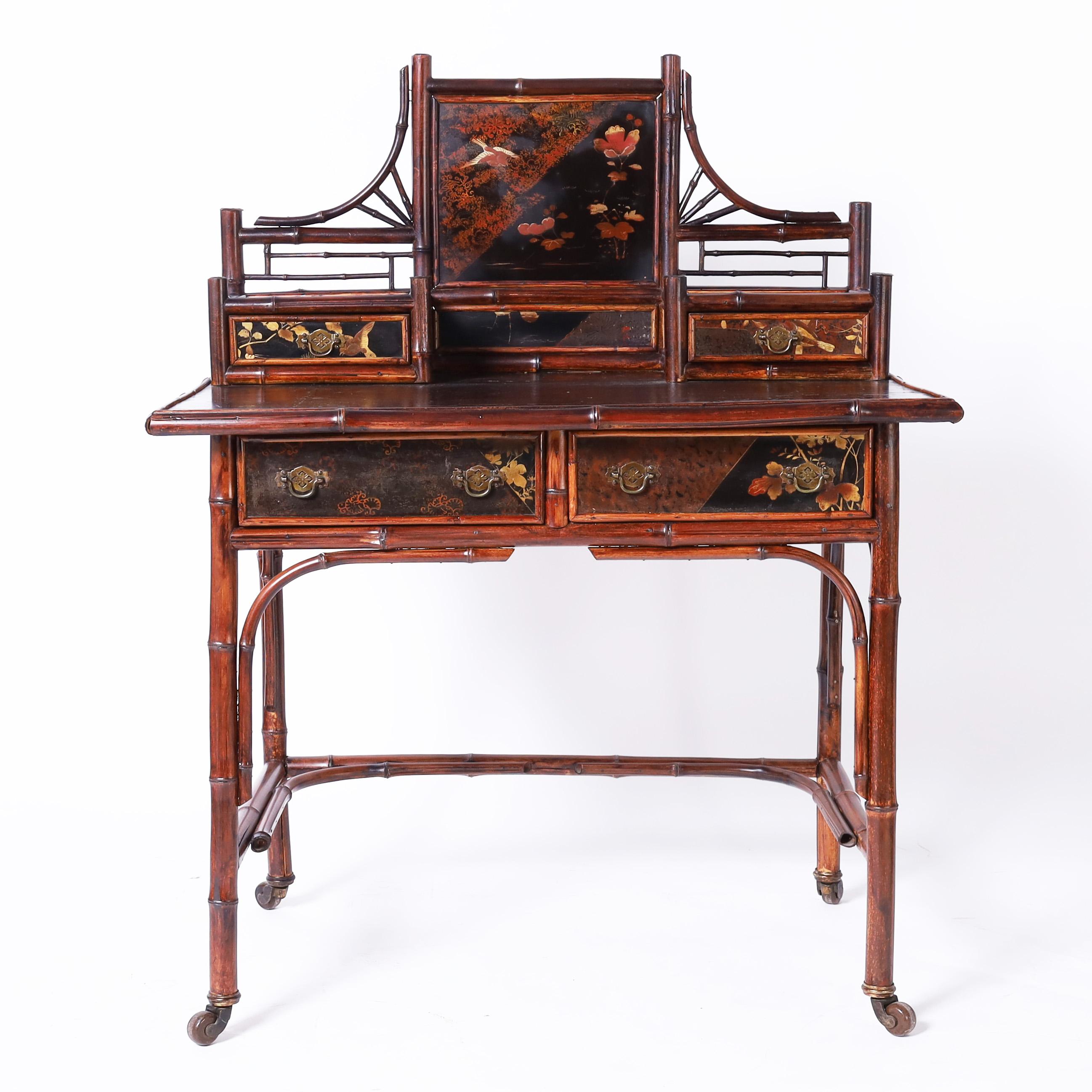 Impressive 19th century English desk handcrafted in bamboo in a Japonisme form featuring lacquered panels hand decorated with flowers and birds, the original brass hardware, leather writing surface and bracketed legs on brass casters with ceramic