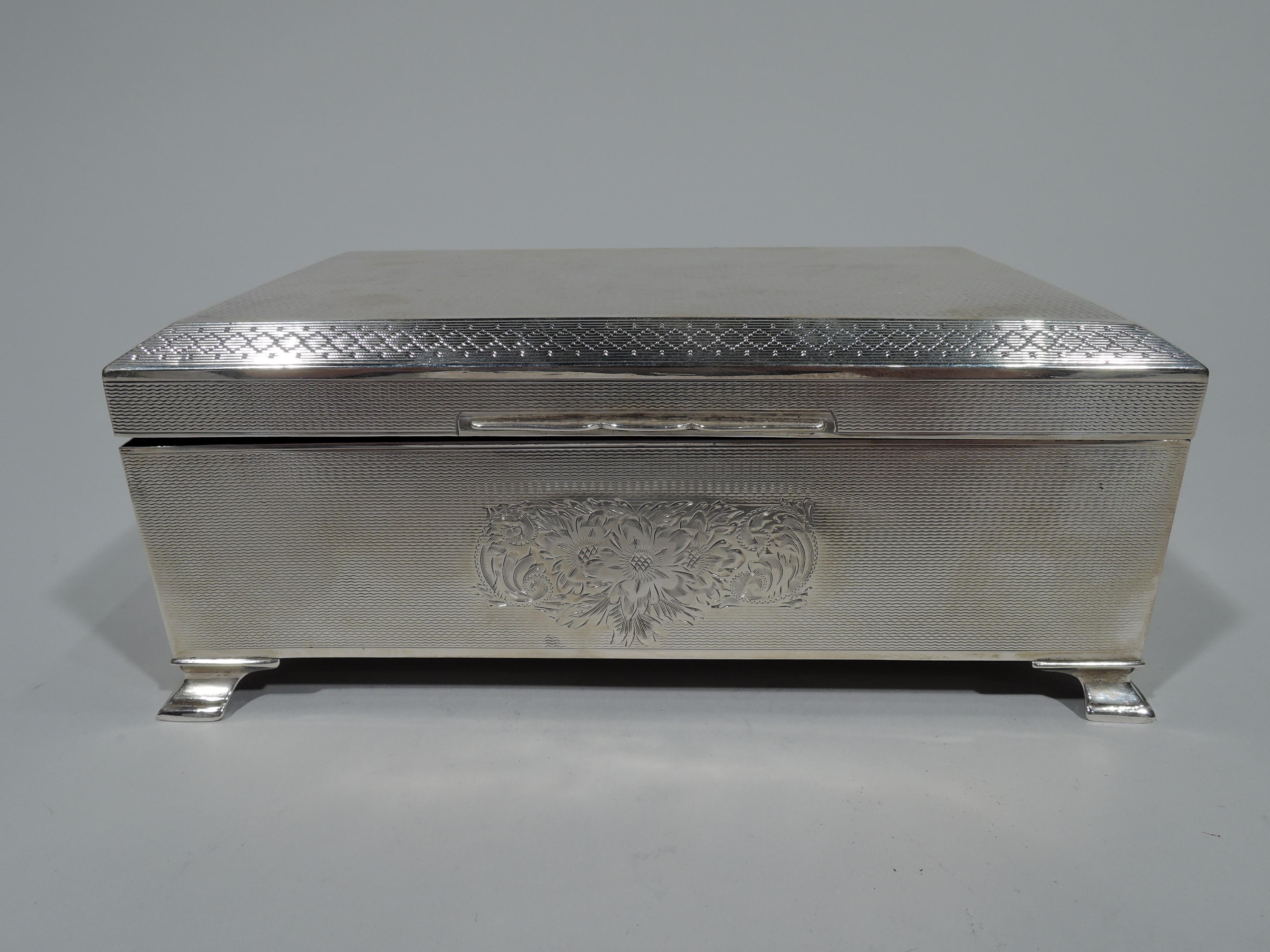 George V sterling silver box. Made by Bert Gordon in Birmingham in 1920 Rectangular with corner bracket supports. Cover hinged and chamfered with scrolled tab. On front engraved flowers and scrolls surrounded by allover engine-turned ornament.