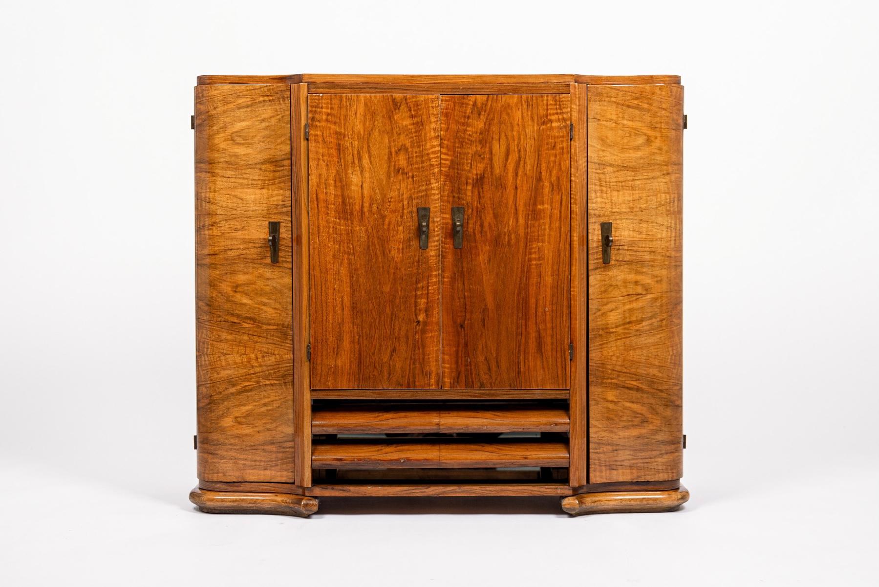 This unique antique English Art Deco wood and glass bar cabinet or sideboard is circa 1930. This smaller cabinet with a distinctive shaped case, curved doors and beautiful opposing wood grain is expertly handcrafted from beech and European walnut