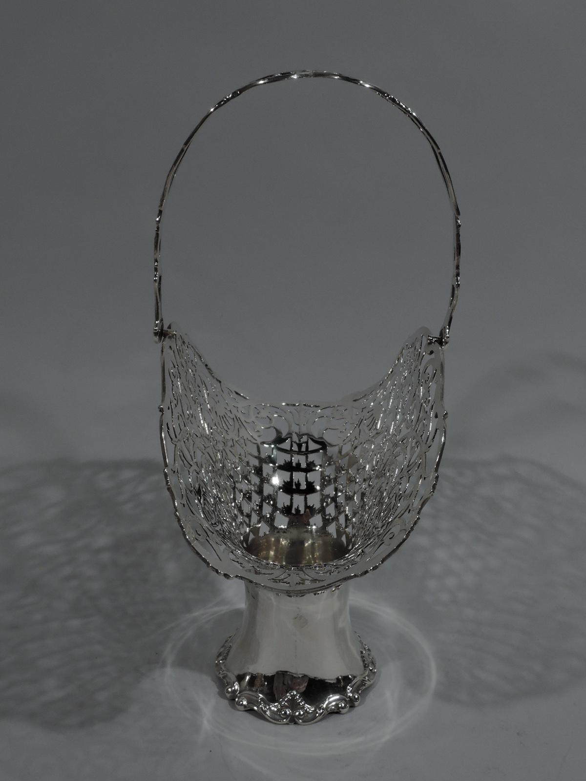Edwardian sterling silver basket. Made by Henry Matthews in Birmingham in 1910. Solid and concave well with applied shell-and-scroll rim. Wide and flattened oval mouth with pierced and stylized scrollwork, flowers, leaves, and diaper. Symmetrical