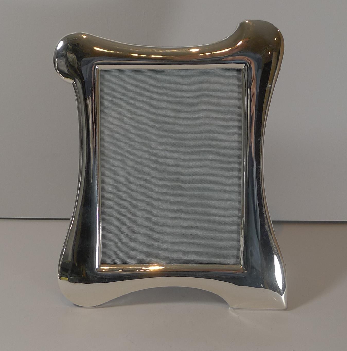 A truly stylish Art Nouveau photograph frame made from English sterling silver with a solid English oak backing incorporating a hinged folding stand.

The organic shape is simply exquisite surrounding the rectangular glazed aperture measuring 5