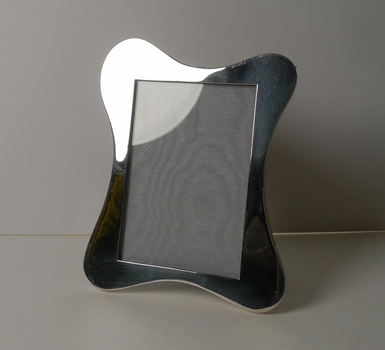 A stylish shaped photograph frame in a decorative Art Nouveau design. Made from solid English silver backed with solid English oak incorporating a folding easel stand.

The silver is fully hallmarked for Birmingham 1914 together with the maker's