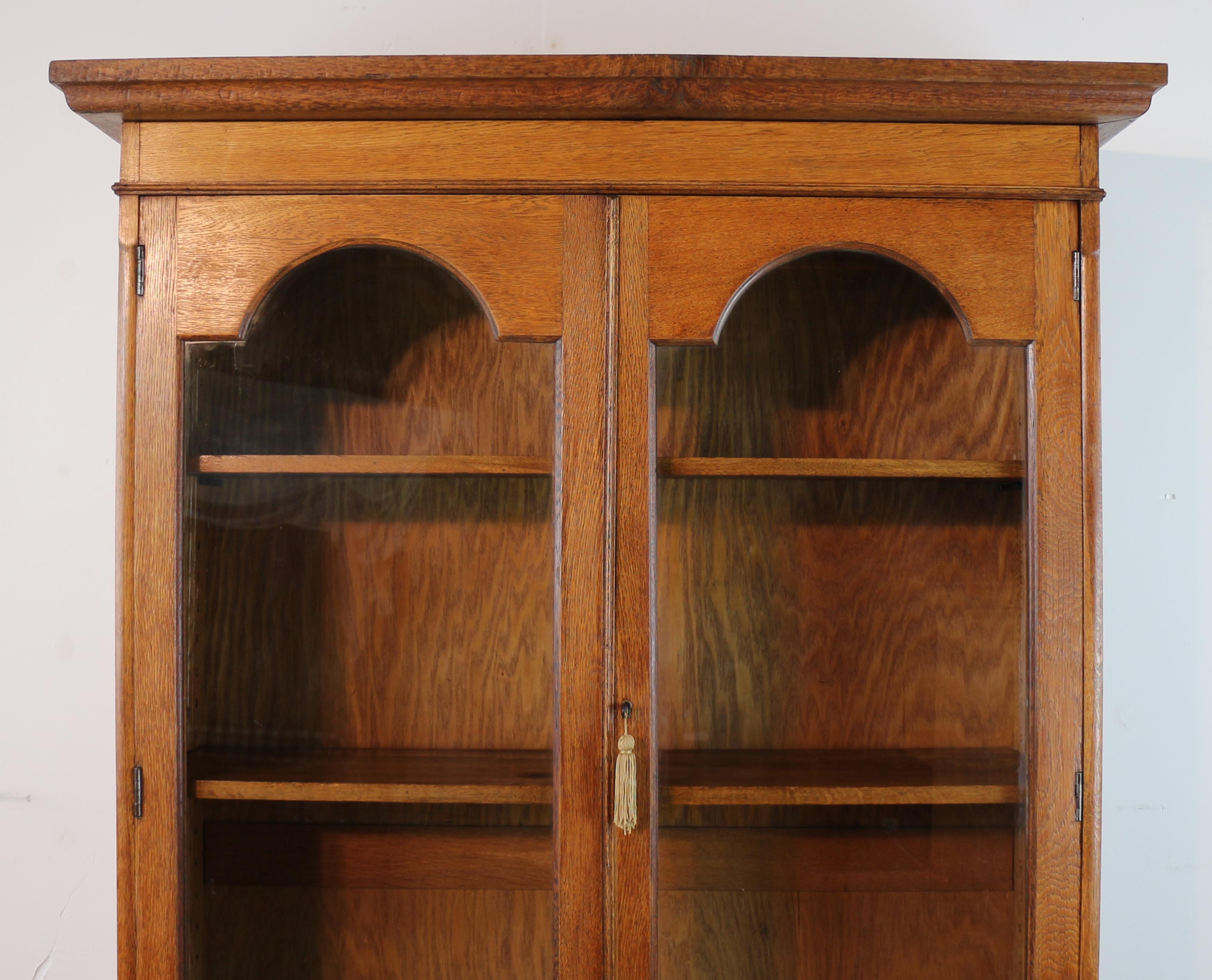 An attractive English Arts & Crafts bookcase cabinet, circa 1900, with pewter, fruitwood and ebonised floral inlay of Art Nouveau style. In golden oak with a moulded cornice above two semi-circular arched glazed upper doors enclosing three