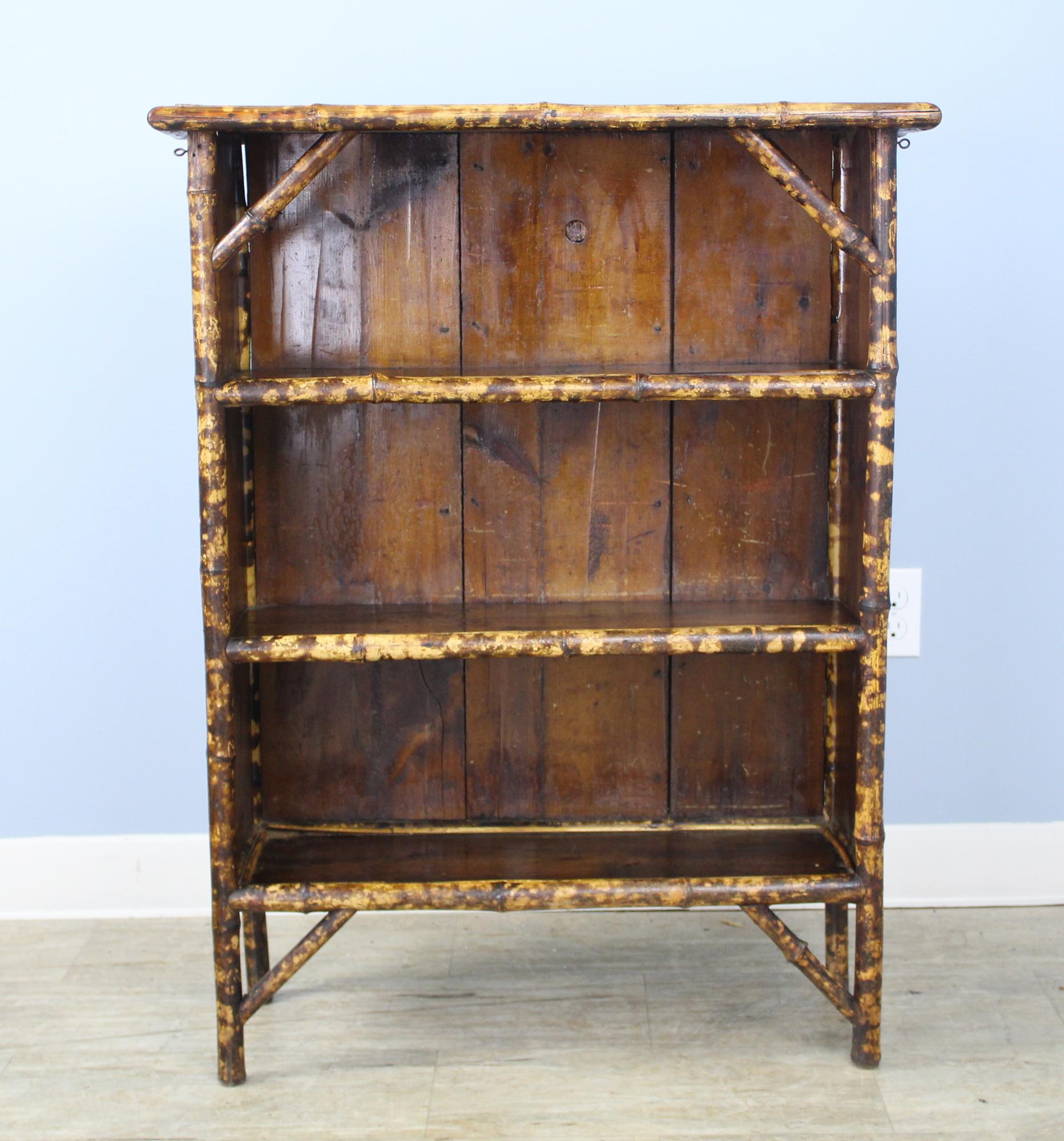 An antique English bookcase fashioned of bamboo, vibrantly colored. The wooden top and back are a rich brown. Very stabile and sturdy for its age.