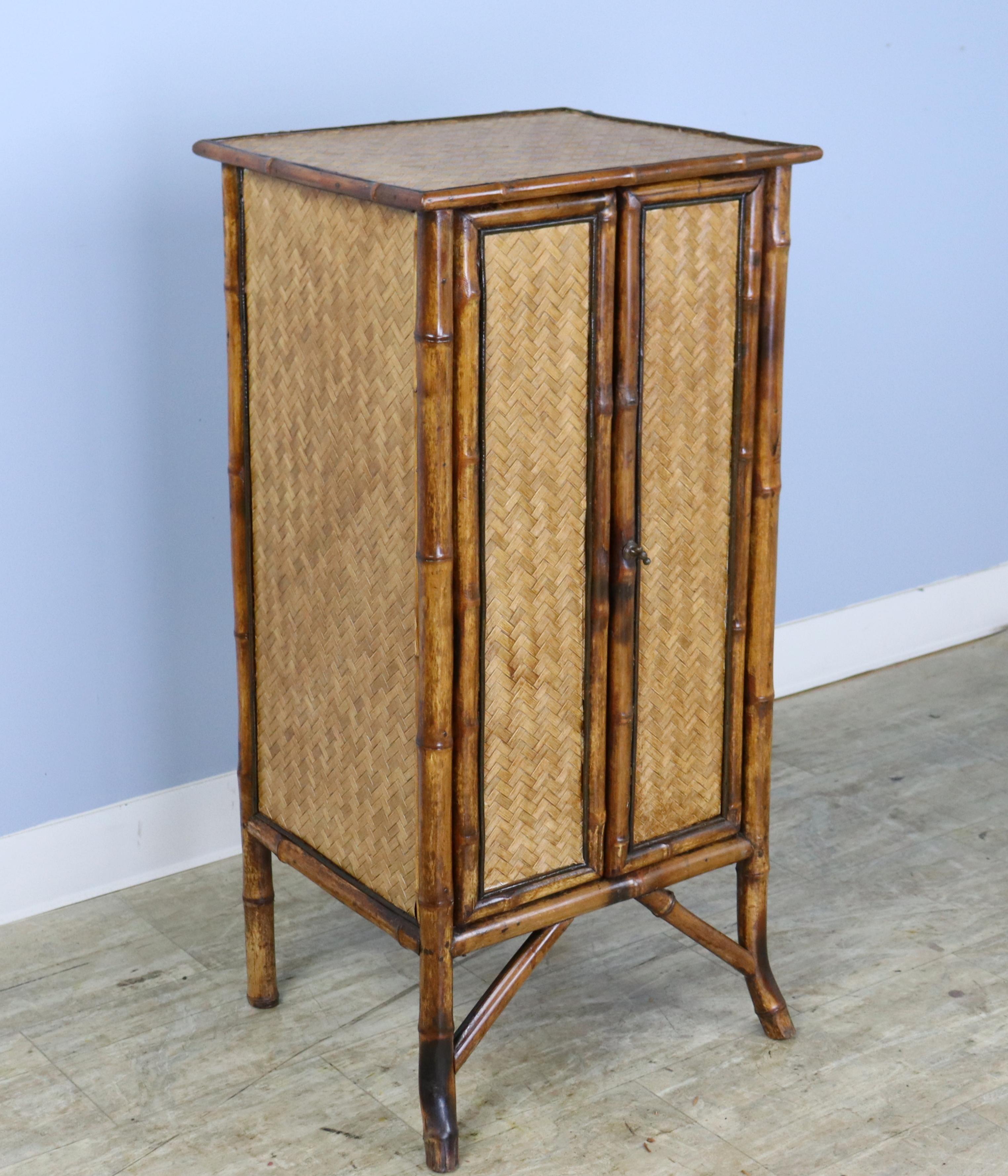 A charming bamboo cabinet with rattan top in very good antique condition. Three interior shelves. The bamboos is vibrant and has great color. Swing closure on right door works well.