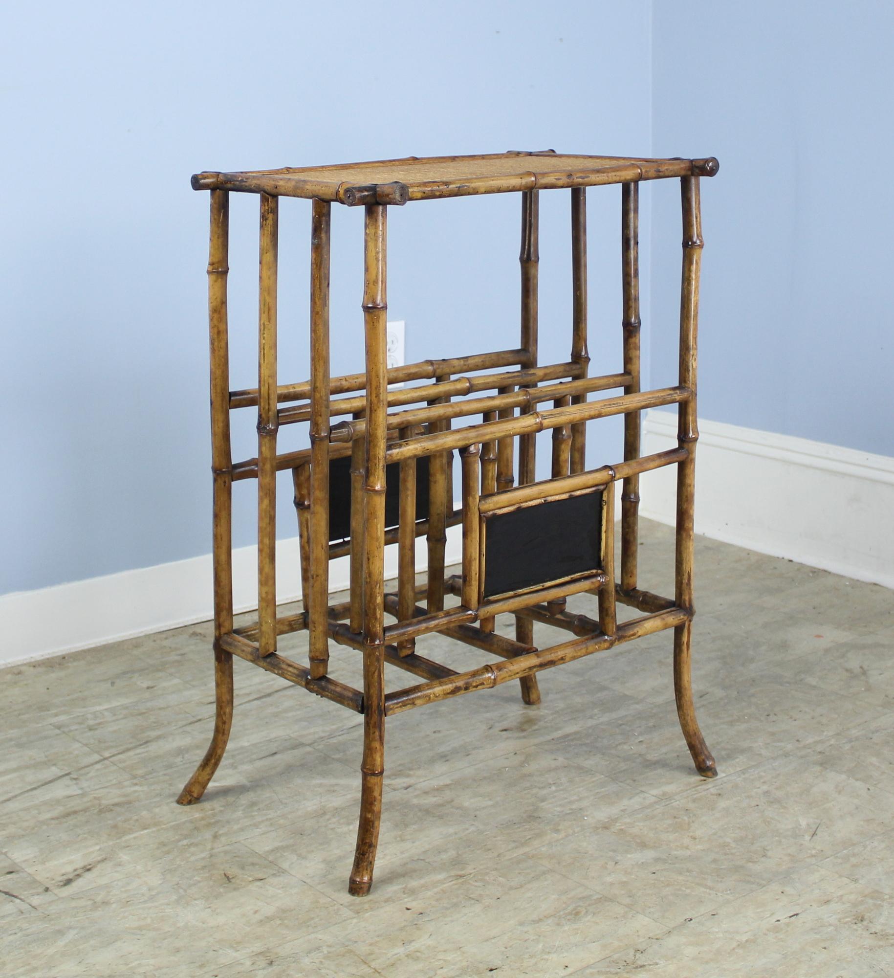 A highly decorative bamboo side or lamp table that is also a useful magazine rack or canterbury, originally designed to hold sheet music. The bamboo is in good antique condition with vibrant color and the rattan top is also in good condition. One