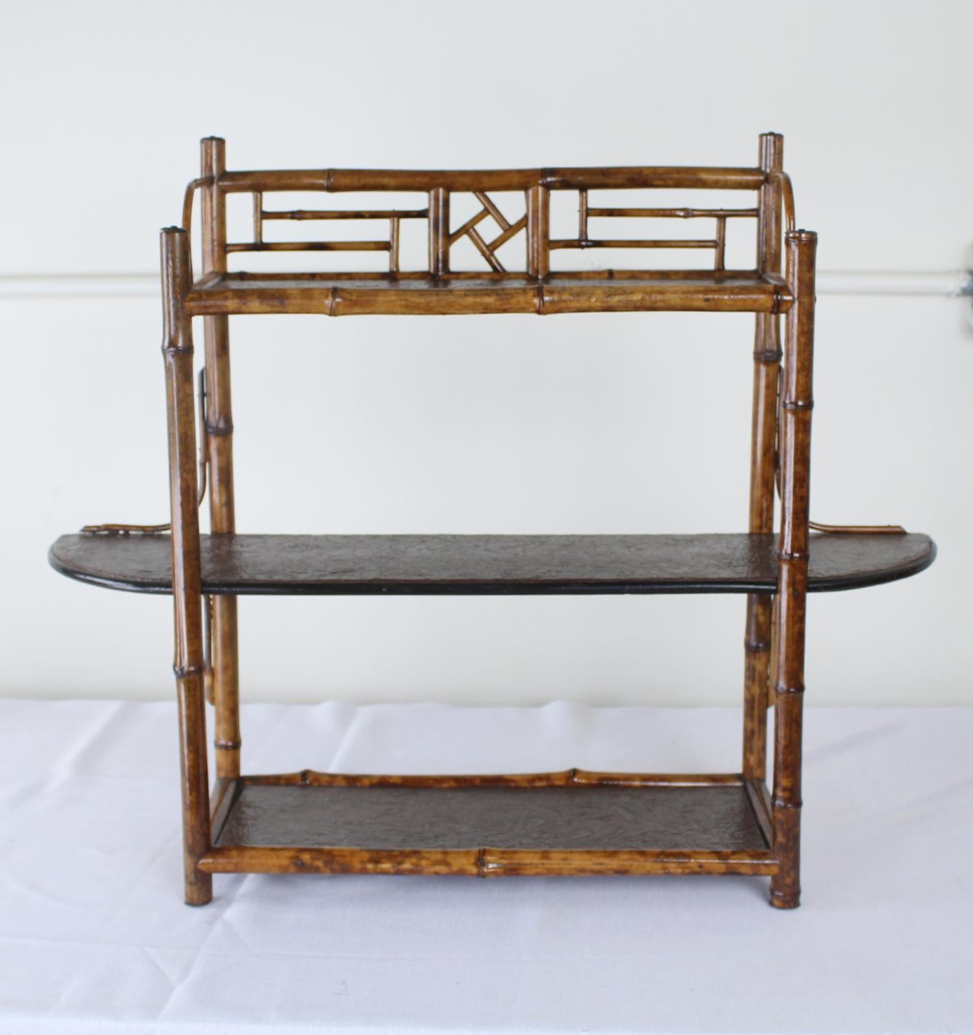 A charming wall or free standing shelf, fashioned of vibrant bamboo. The small detail pieces are all intact, and the pressed leather on the shelves is in good condition.