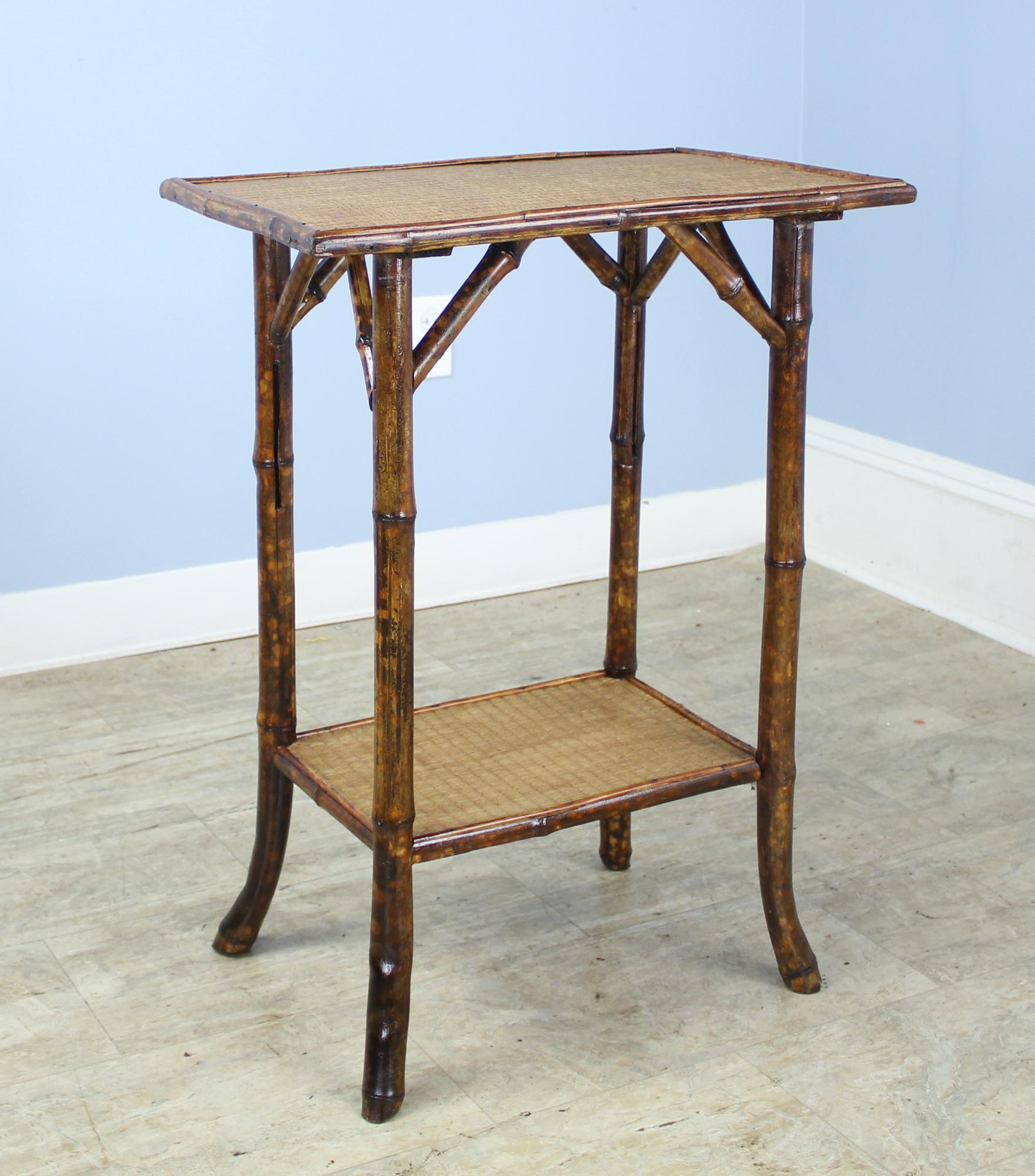 An antique English bamboo side table, with flared legs and with two shelves. Both shelves are made of tightly woven rush that is in very good condition. The bamboo, vividly painted, is in good sturdy condition. Charming as an end or lamp table.