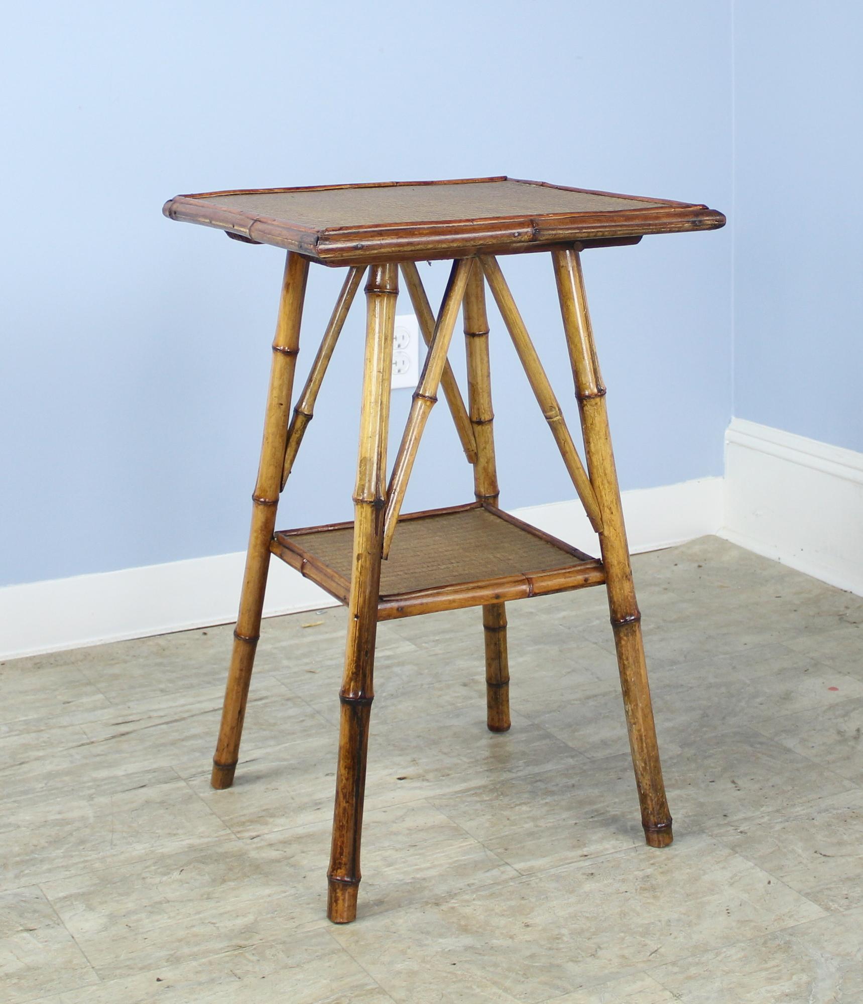 An antique English bamboo side table, with flared legs and with two shelves. Both shelves are made of tightly woven rattan that is in very good condition. The bamboo, vividly colored, is in good sturdy condition. Charming as an end or lamp table.