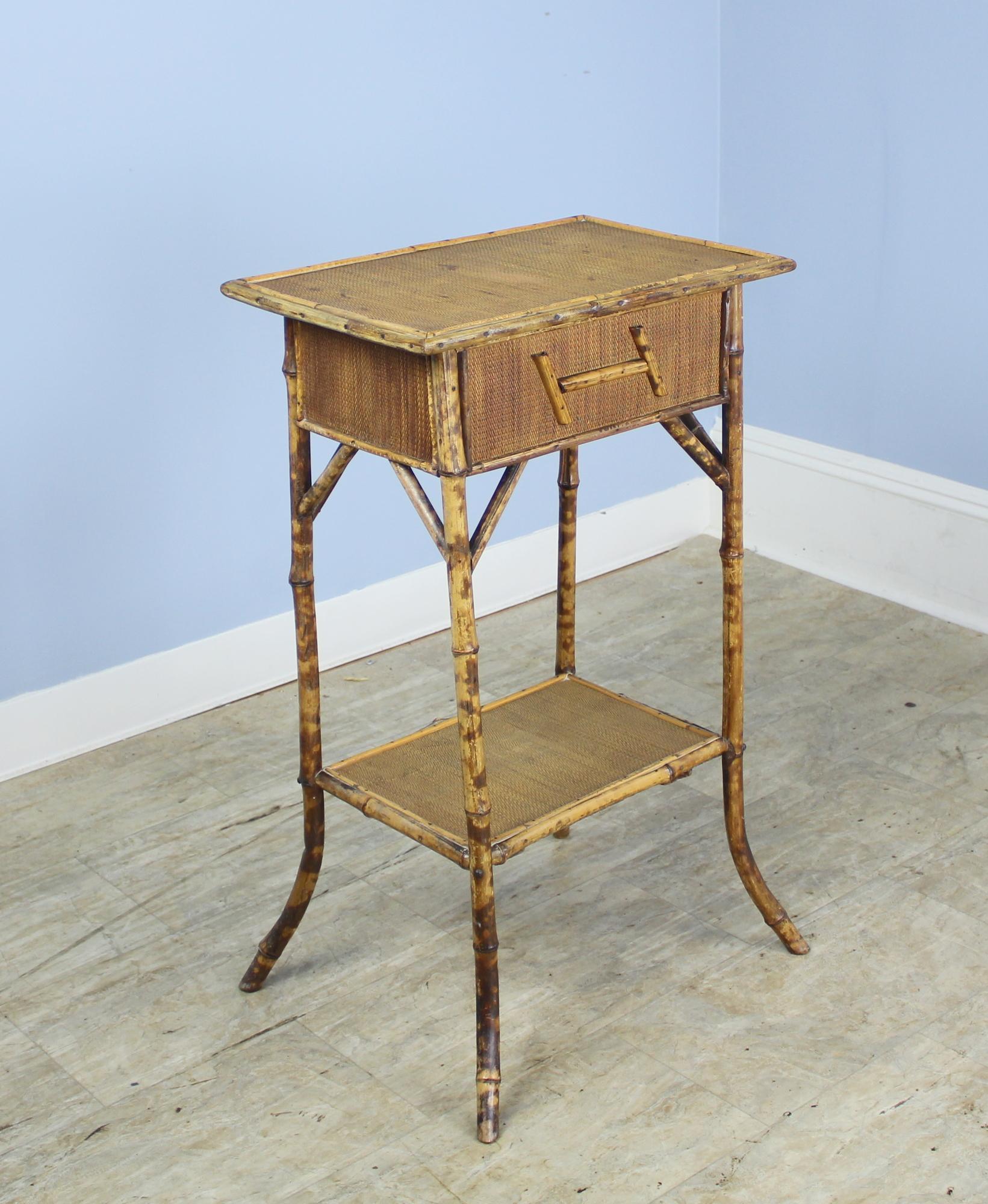 An attractive antique bamboo side table, originally a sewing box on flared legs. The box lifts from one hinged side, and is lined with old paper. The H shaped decoration on the outside is the same on both front and back. A delicate and charming side