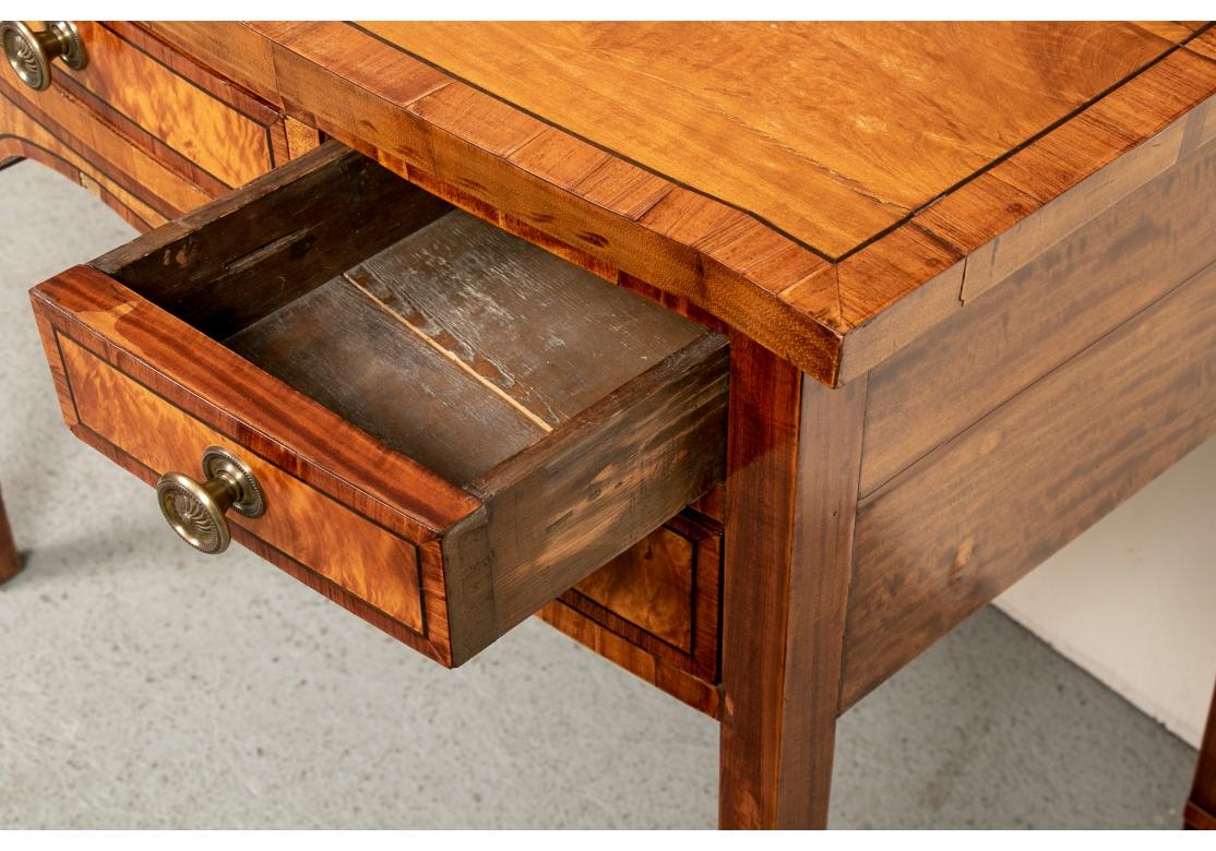The banded top with thin ebonized string inlays. The slightly shaped front with a knee hole.The apron with a center drawer flanked by double drawers, all banded and burled. With fine cast brass knob pulls with sunburst motifs. With two part burled