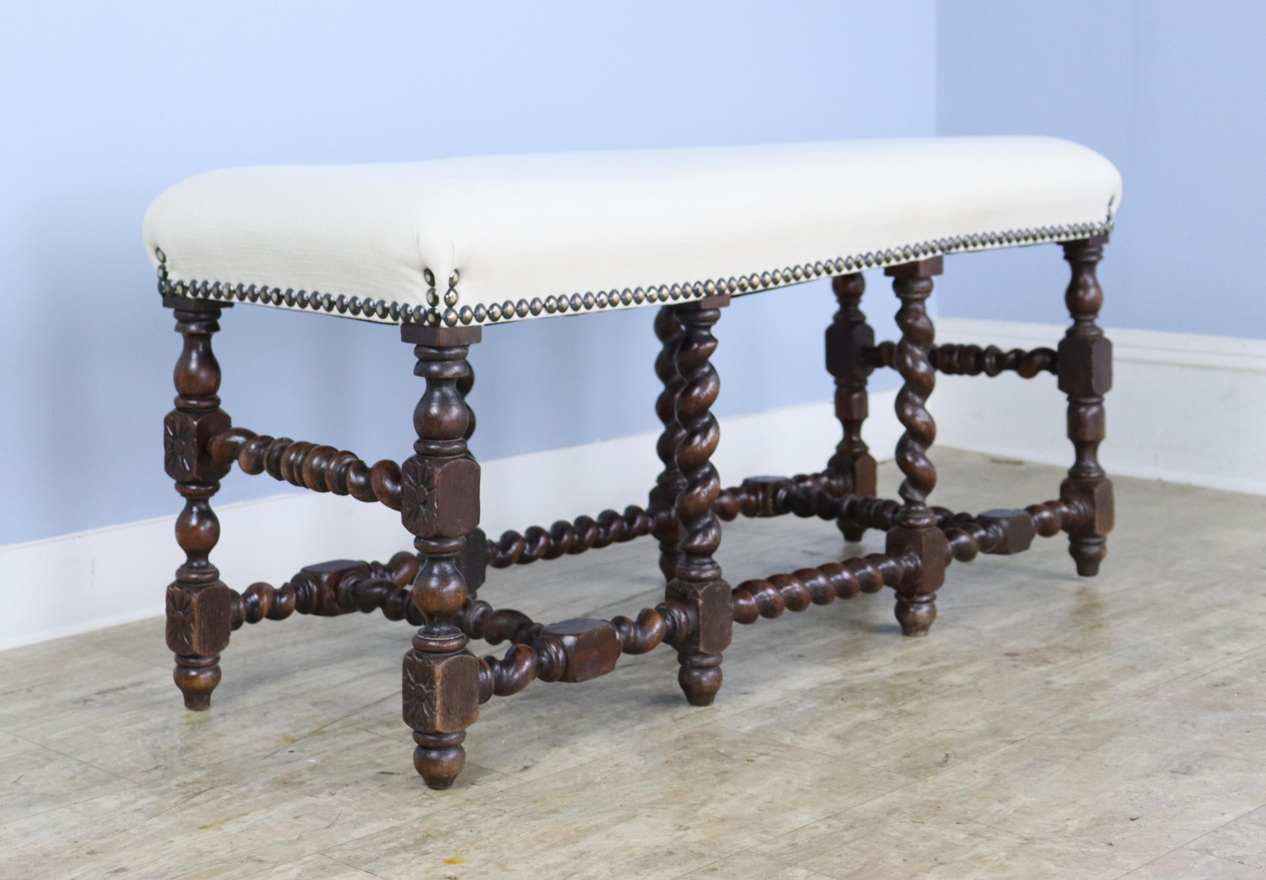 A long stool or bench with visually arresting oak barley twist supports. Good nail head detail where the seat meets the legs. Newly upholstered in white muslin to be used as is or reupholstered.  There is an area where the original handmade