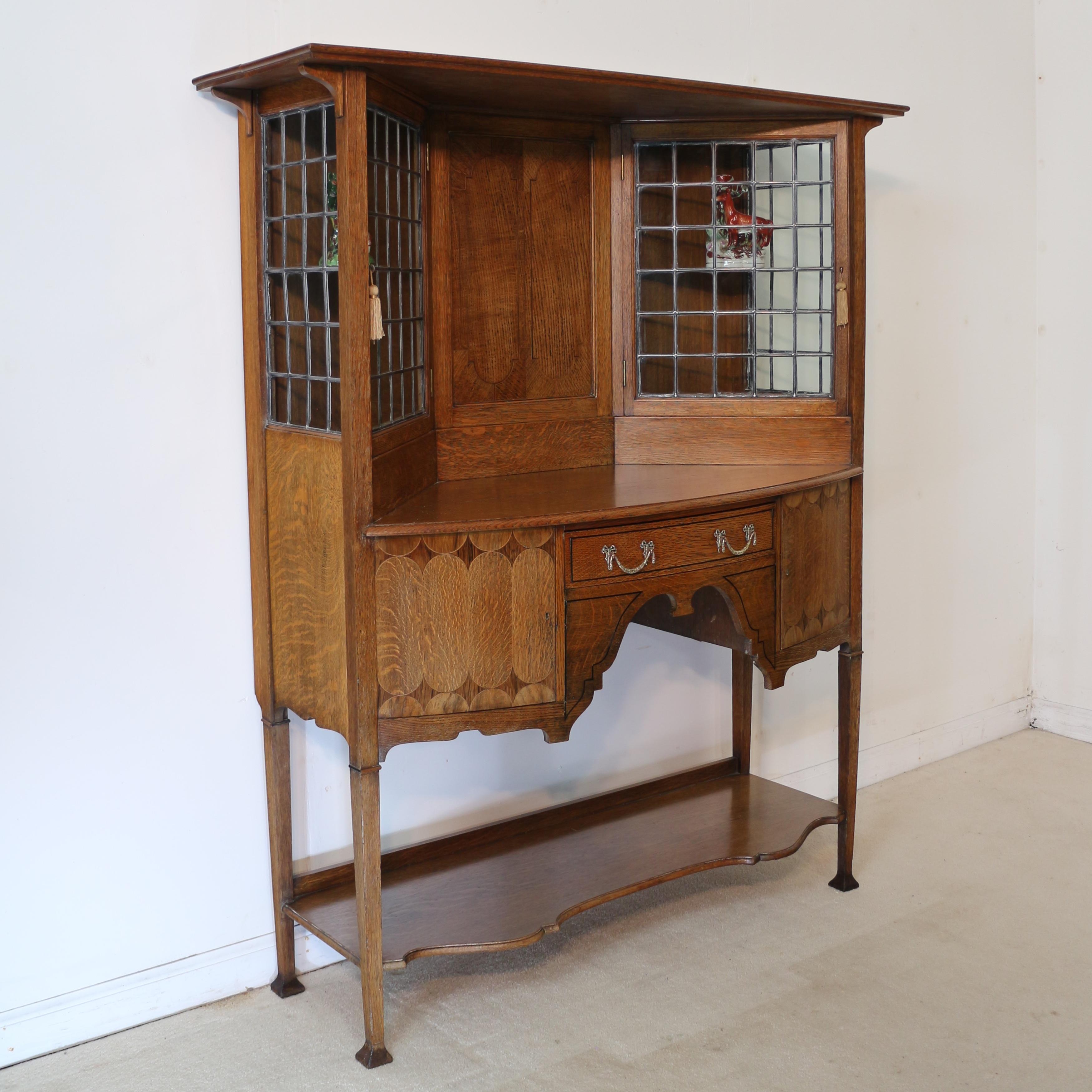An unusual Arts & Crafts quarter-sawn oak & marquetry bowfront sideboard cabinet by Bath Cabinet Makers. Dating to circa 1895 this beautiful side cabinet is of neat proportions and features a flared rectangular cornice above an inlaid panelled back