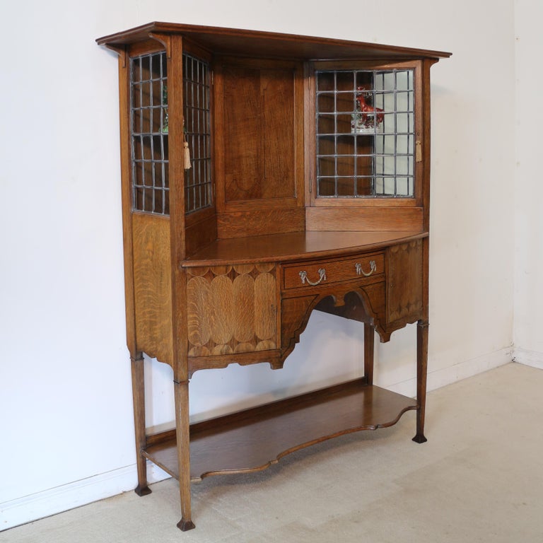An unusual Arts & Crafts quarter-sawn oak & marquetry bowfront sideboard cabinet by Bath Cabinet Makers. Dating to circa 1895 this beautiful side cabinet is of neat proportions and features a flared rectangular cornice above an inlaid panelled back