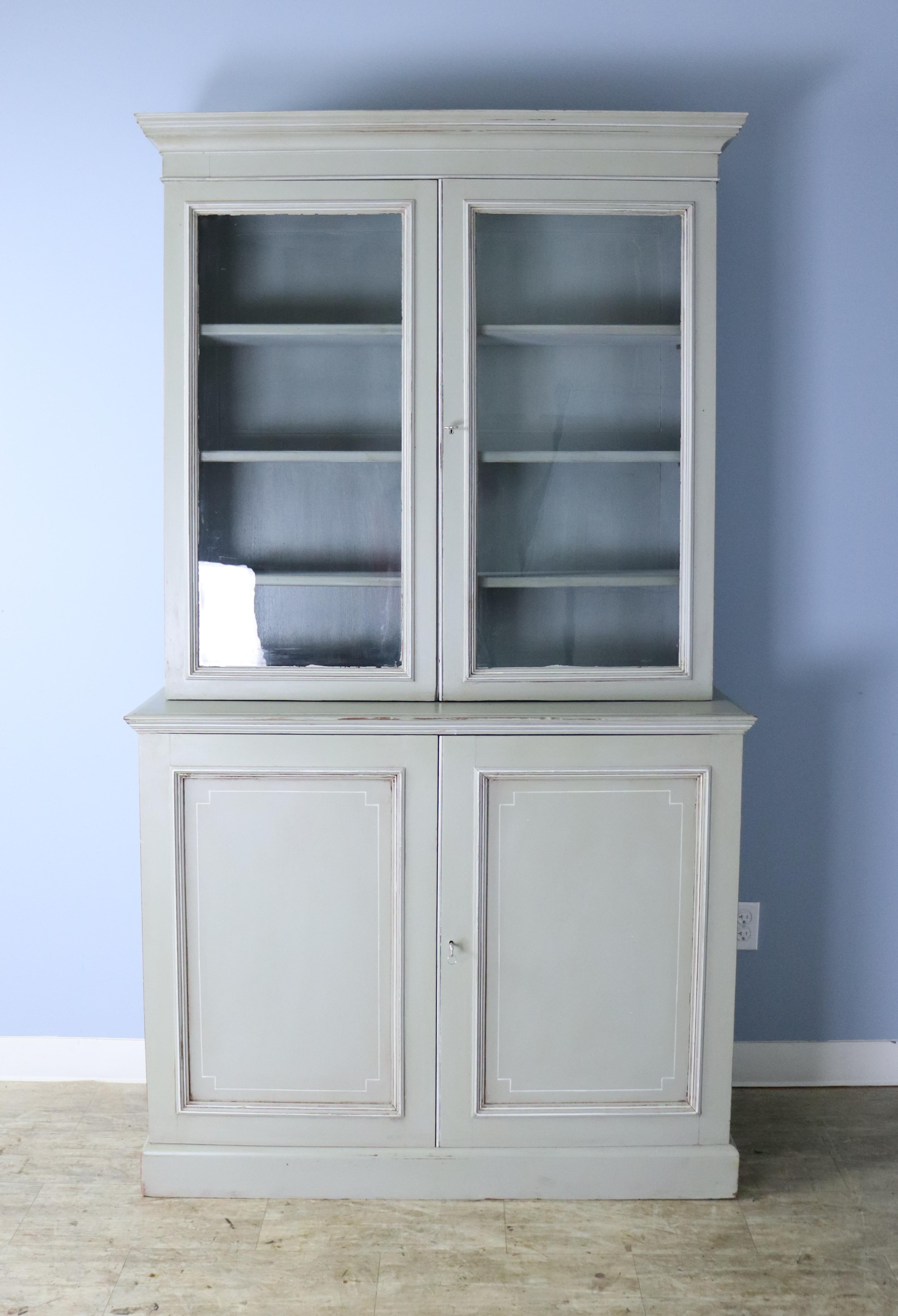 A two piece bookcase or cabinet from the later half of the 19th century but newly painted a pale green in the Regency style with faux distress. Both the top section and the bottom have non adjustable shelves with plenty of good storage. The bottom
