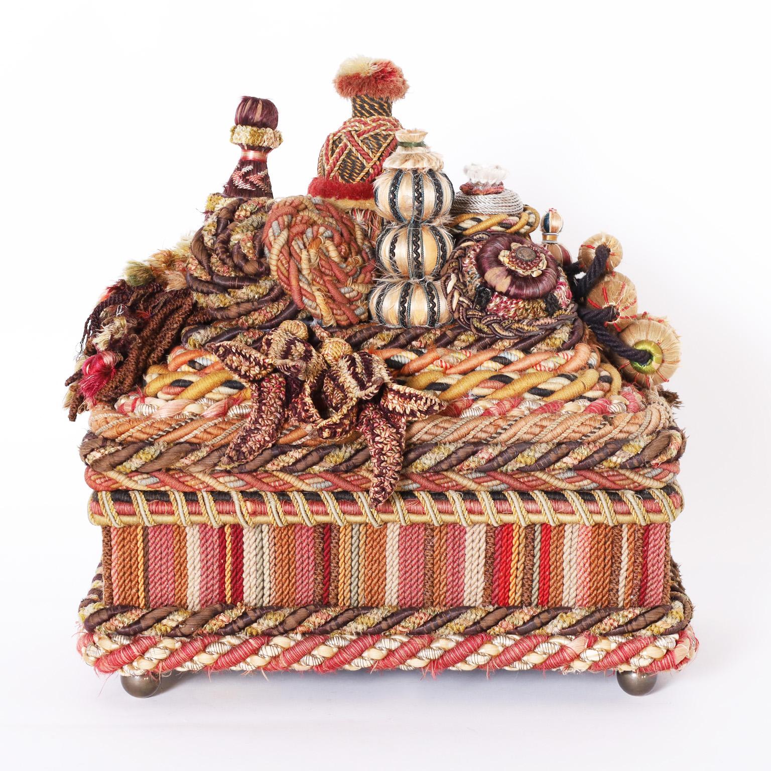 Standout 19th century English box crafted in mahogany and decorated with an eccentric multi layered composition of braids, tassels and bulbs all in remarkable condition and set on brass ball feet.