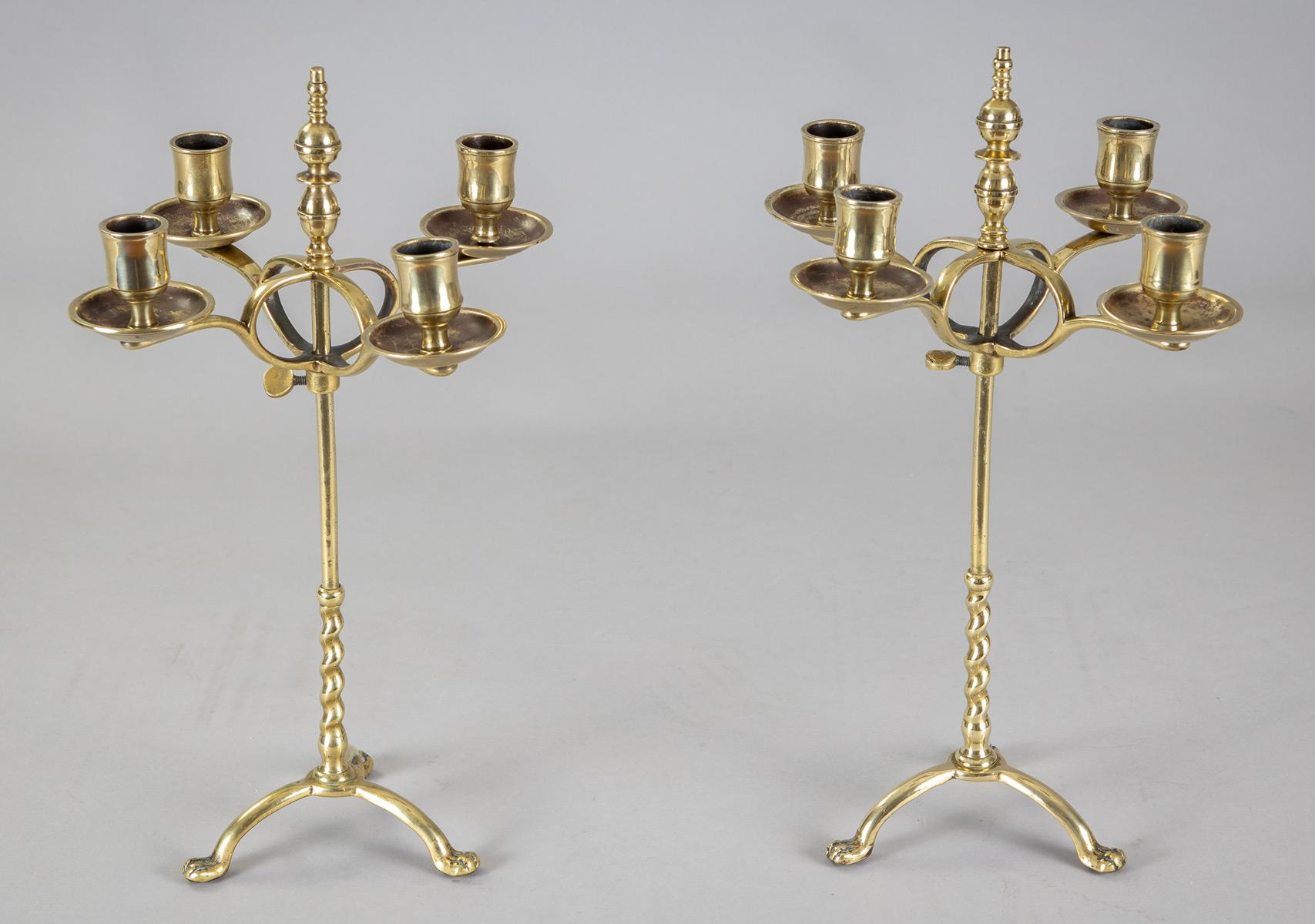Antique pair of English brass four-light adjustable candelabra, the central stem on a barley twist column, turned brass finial, wing nut to raise, lower and tighten the cluster, mounted on tripod base ending in paw feet.