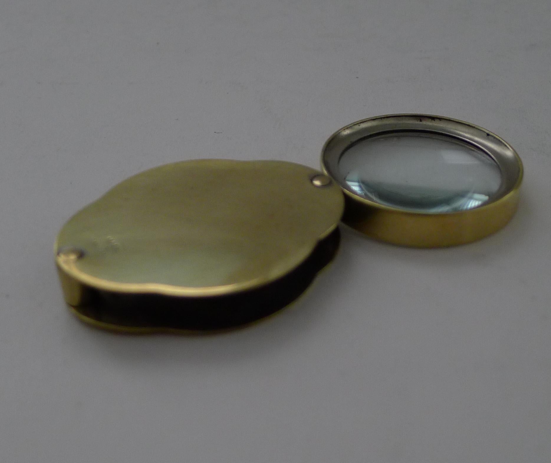 A lovely shaped little folding / pocket magnifying glass which folds into a shaped brass case, marked 