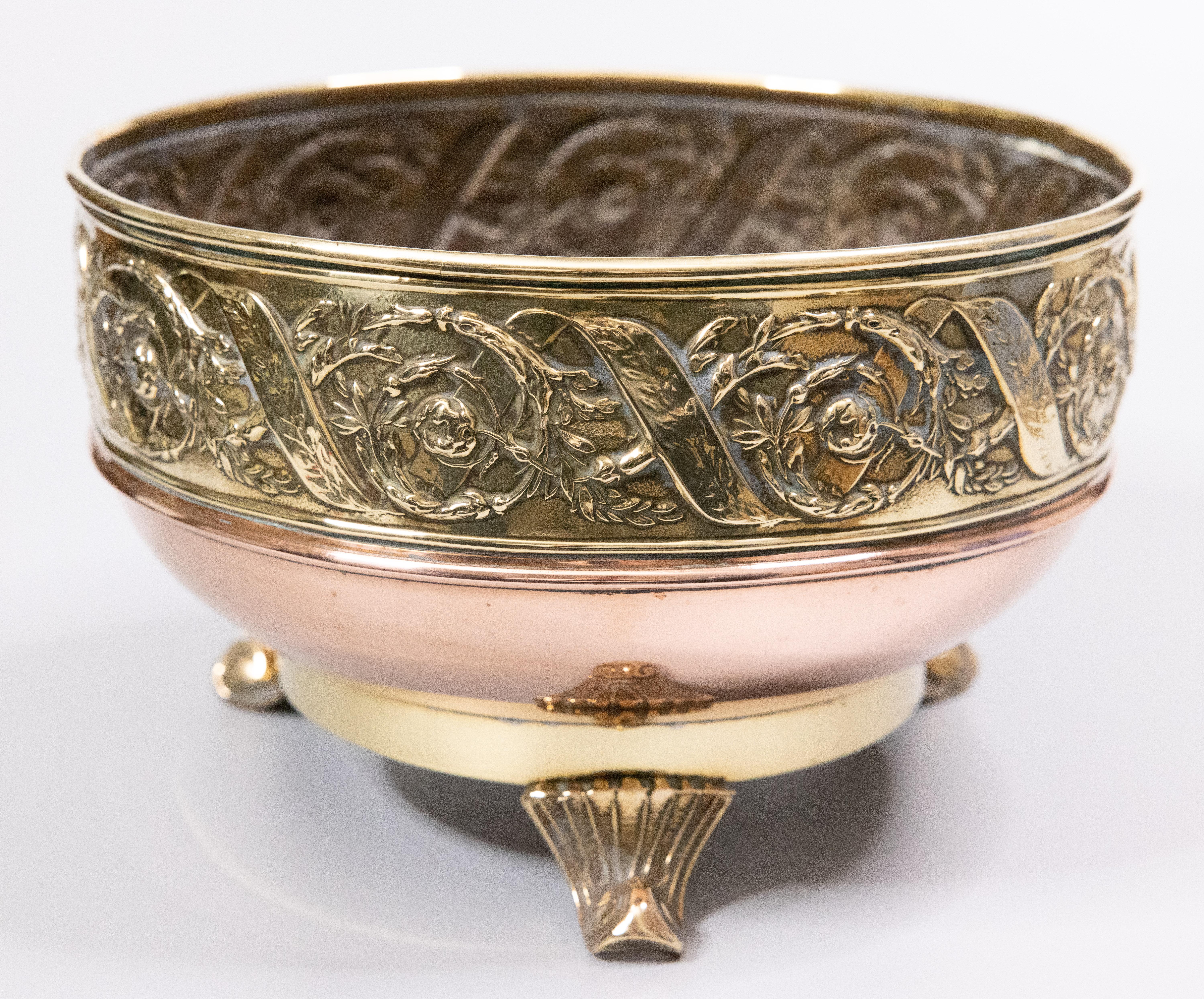 A gorgeous antique English brass and copper footed jardiniere / planter / cachepot / bowl, circa 1920. This fine pot is handcrafted of copper with a brass repoussé floral design and ornate brass feet. It would be lovely displayed on its own, filled