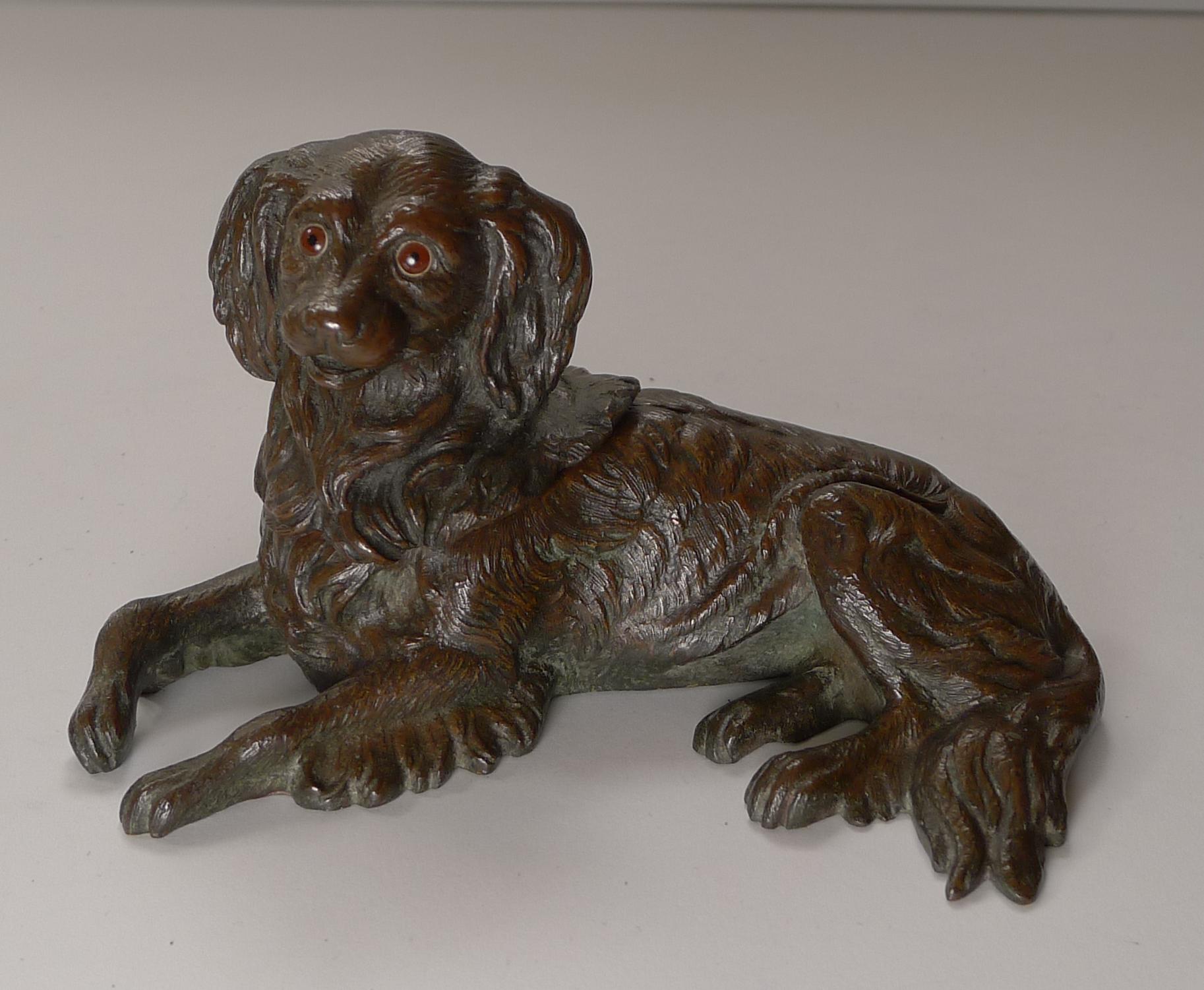 A handsome Victorian novelty inkwell, cast in bronze in the form of a King Charles Spaniel, beautifully executed with two lovely glass eyes.

The underside is inscribed with a roman numeral IV. The hinged head lifts to reveal a removable glass ink