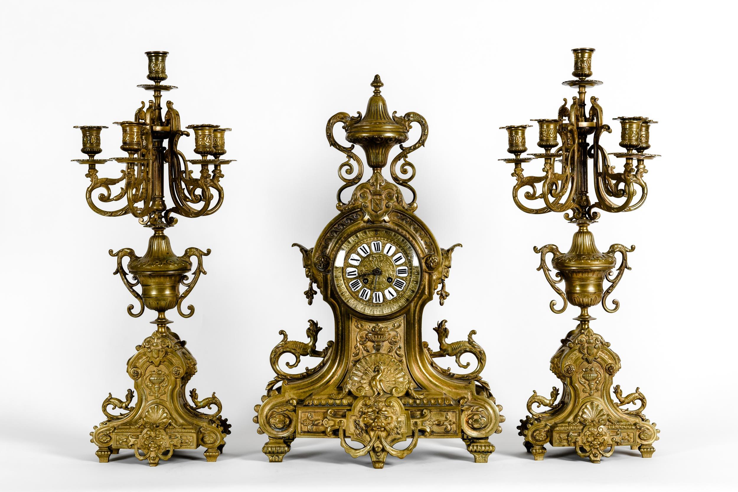 Antique English bronze renaissance revival three-piece clock garniture. The set composed of a center clock and two flanking six arms candelabra. Each piece is lavishly decorated with lion heads, winged caryatid, and serpents. Accented overall with