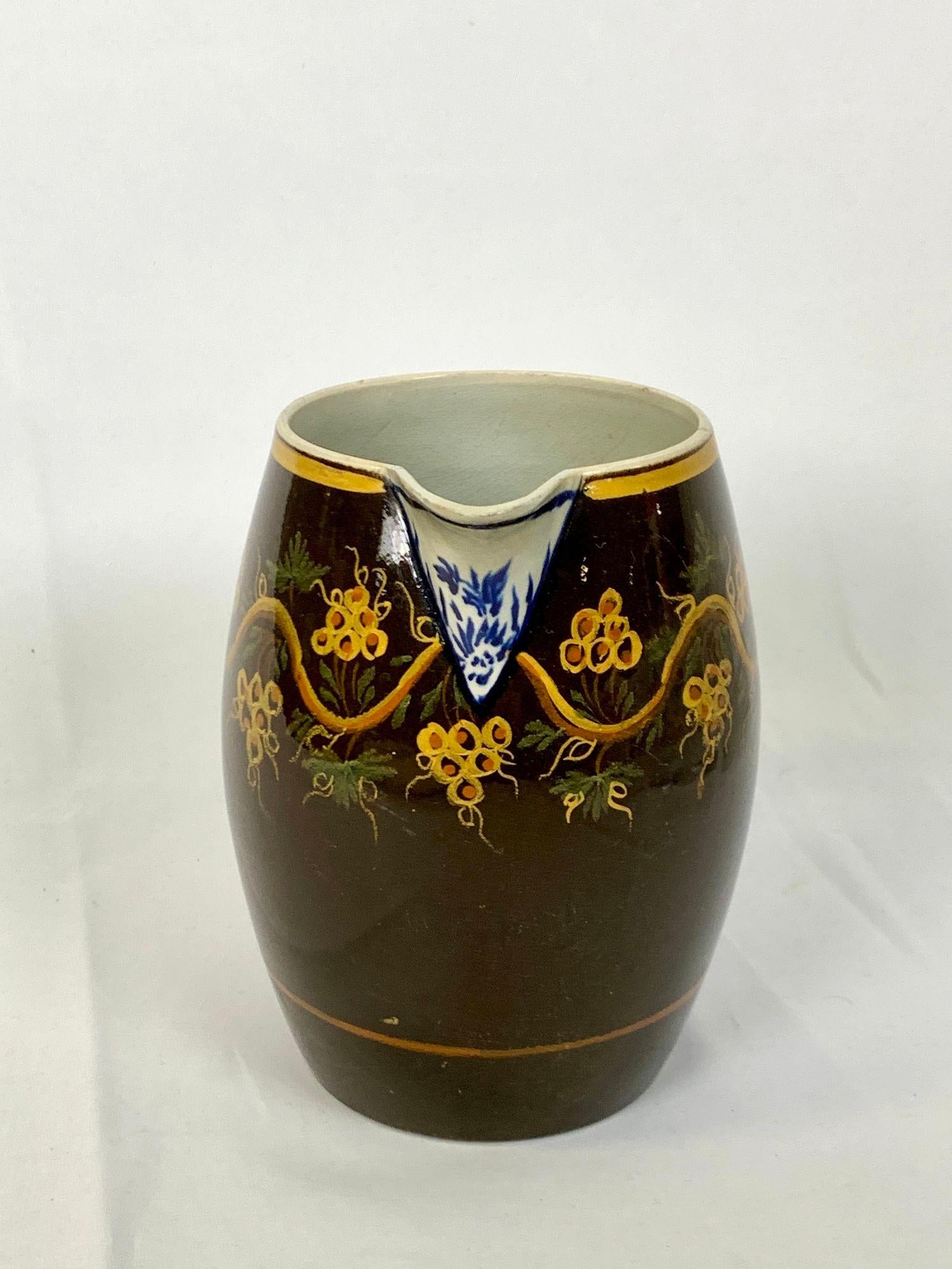 Questa antica brocca inglese, risalente al 1810 circa, è un raro esempio di cremeria decorata a scivolo che evoca lo spirito della moka ma si discosta dal suo aspetto tipico.
Invece di presentare i motivi dendritici o a bande comuni nelle ceramiche