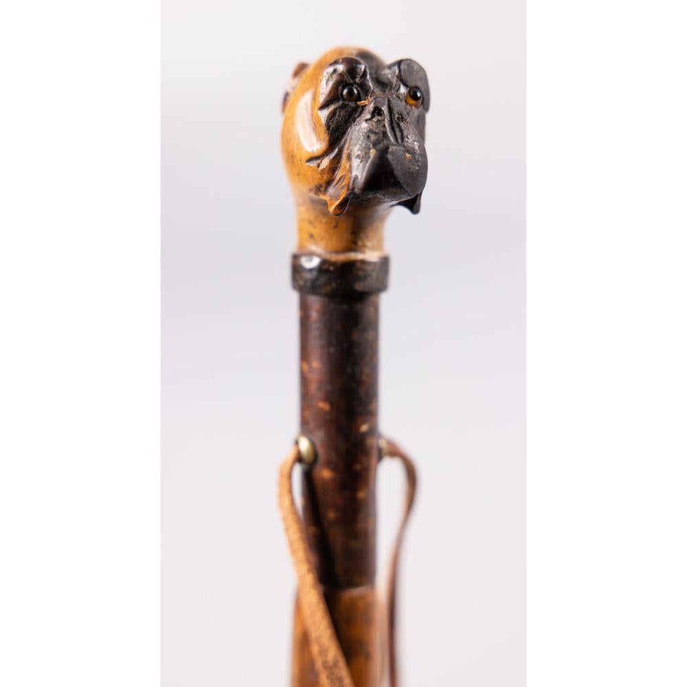 A superb antique 19th Century English walnut walking stick with a carved dog head handle. This handsome walking stick has a finely carved bulldog handle with glass eyes, knobby wood shaft, and leather strap for hanging. It is functional and