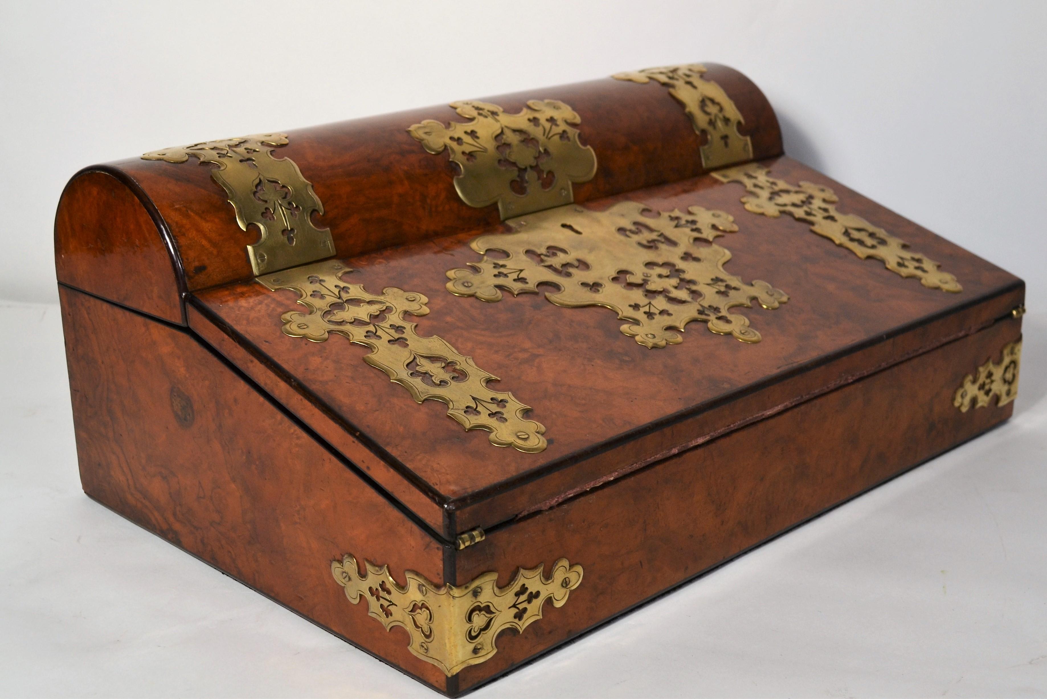 This burl lap desk is in very good shape considering its age.  The nice blood red leather inside is in fine form, with the graceful fleur de lis elements at each corner, as is the leather pull to expose the storage area.  There is a key for this lap