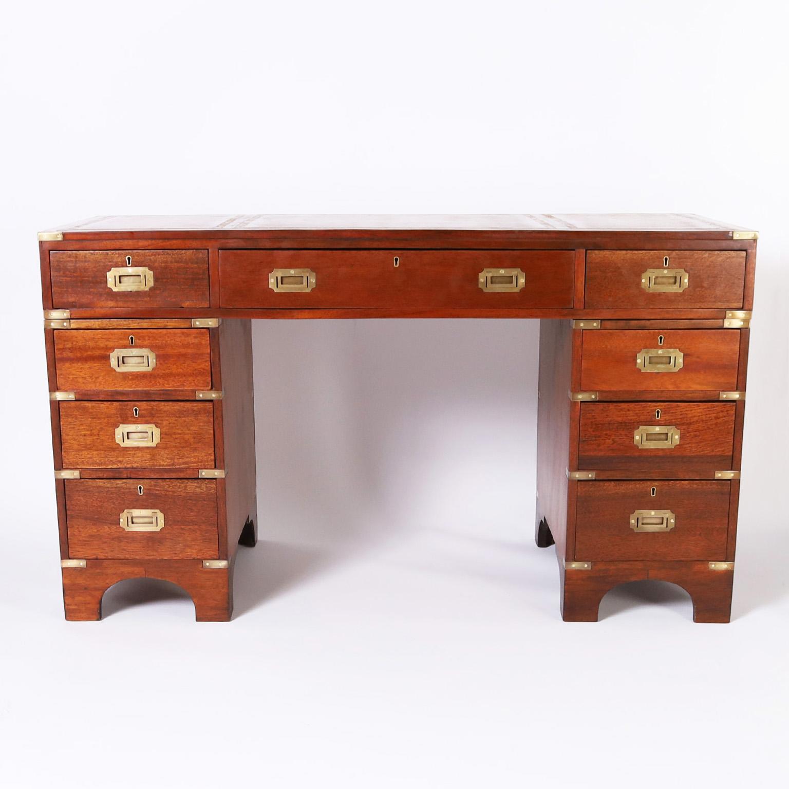 Handsome antique English British Colonial campaign desk crafted in mahogany, in three pieces, with a lush tooled brown leather top, nine drawers, brass campaign hardware and arched feet.