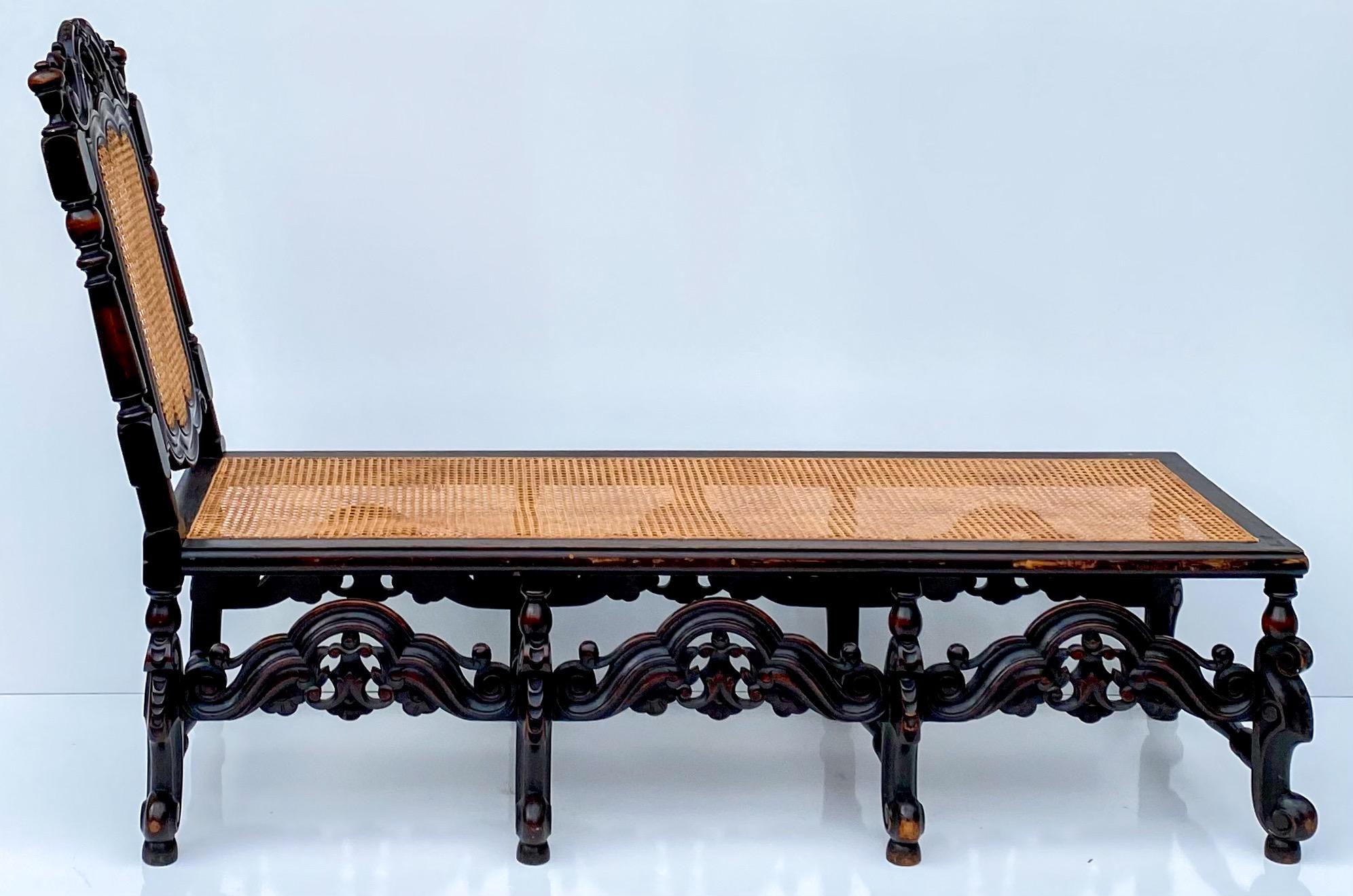 This is a late 19th century carved oak and cane William and Mary style chaise. The carved arched stretchers are intact and solid as is the cane. It is unmarked and in very good condition.