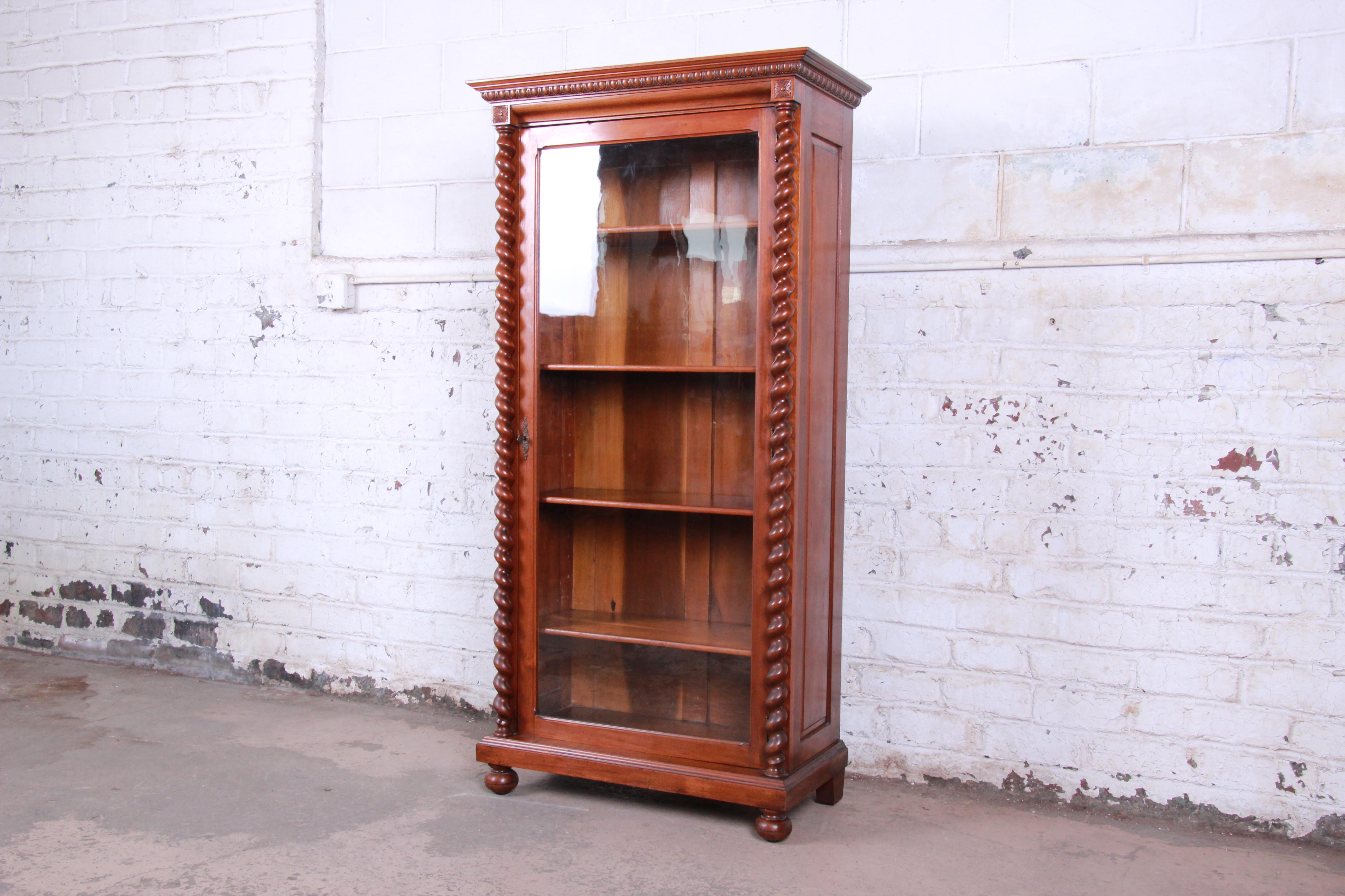An exceptional antique English solid walnut glass front bookcase, circa 1900. The bookcase features beautiful walnut wood grain and nice carved wood details, including barley twist columns on each side. It offers ample storage, with four adjustable