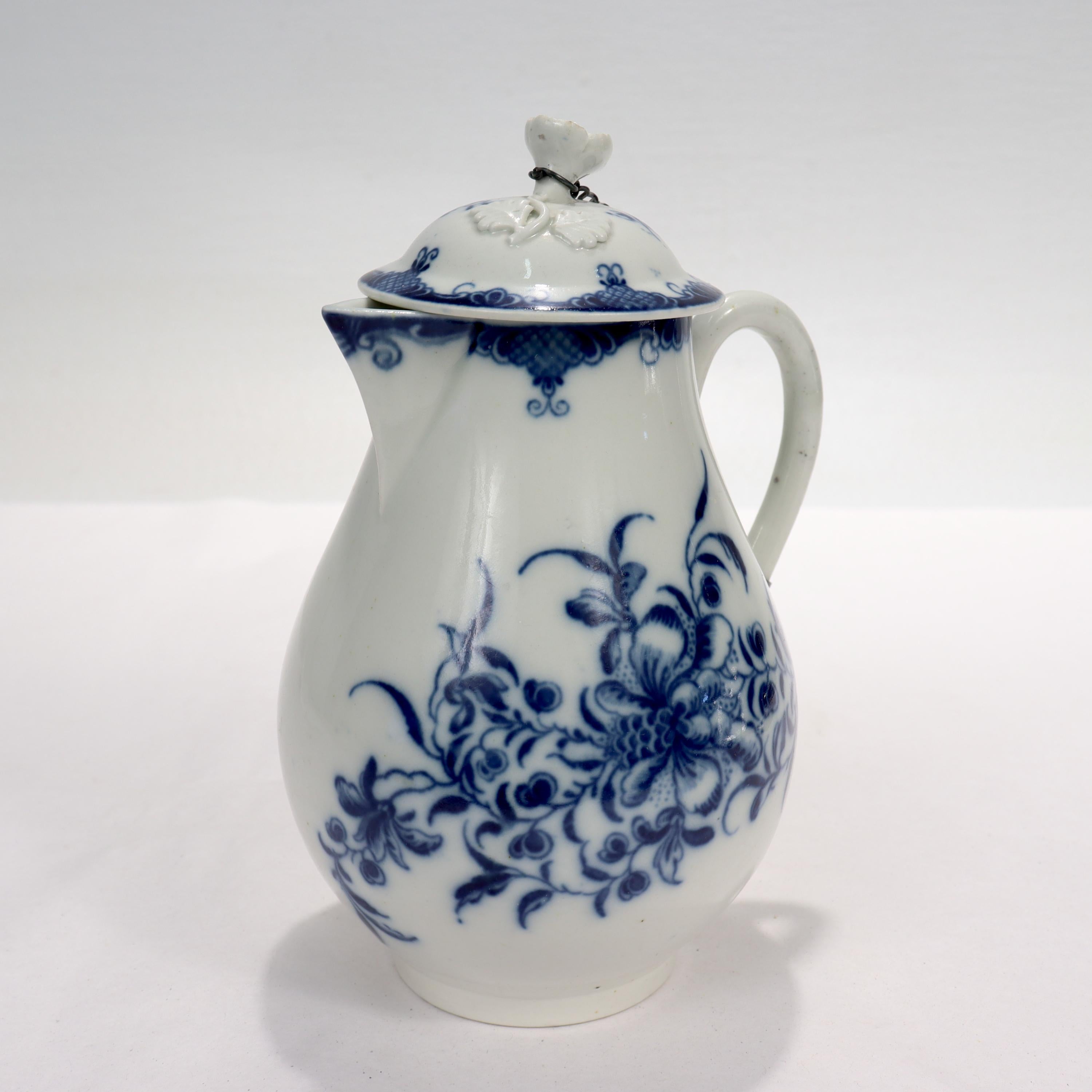 A fine antique English porcelain milk pitcher or jug.

Comprising the pot, a conforming lid, and a later associated chain connecting the two. 

With blue underglaze decoration of floral sprays and a three dimensional flower finial to the