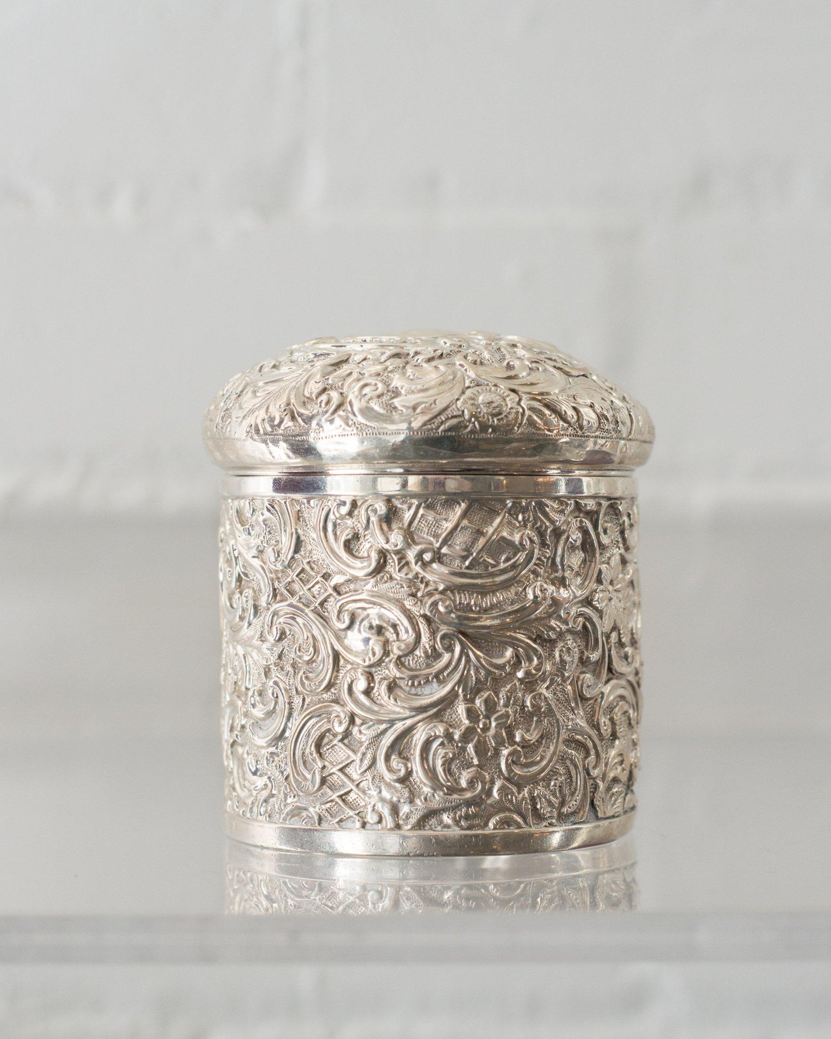 An ornate antique English chased sterling silver container with a lid. A collection of small silver items in a kitchen or bathroom will add a touch of elegance to a room.