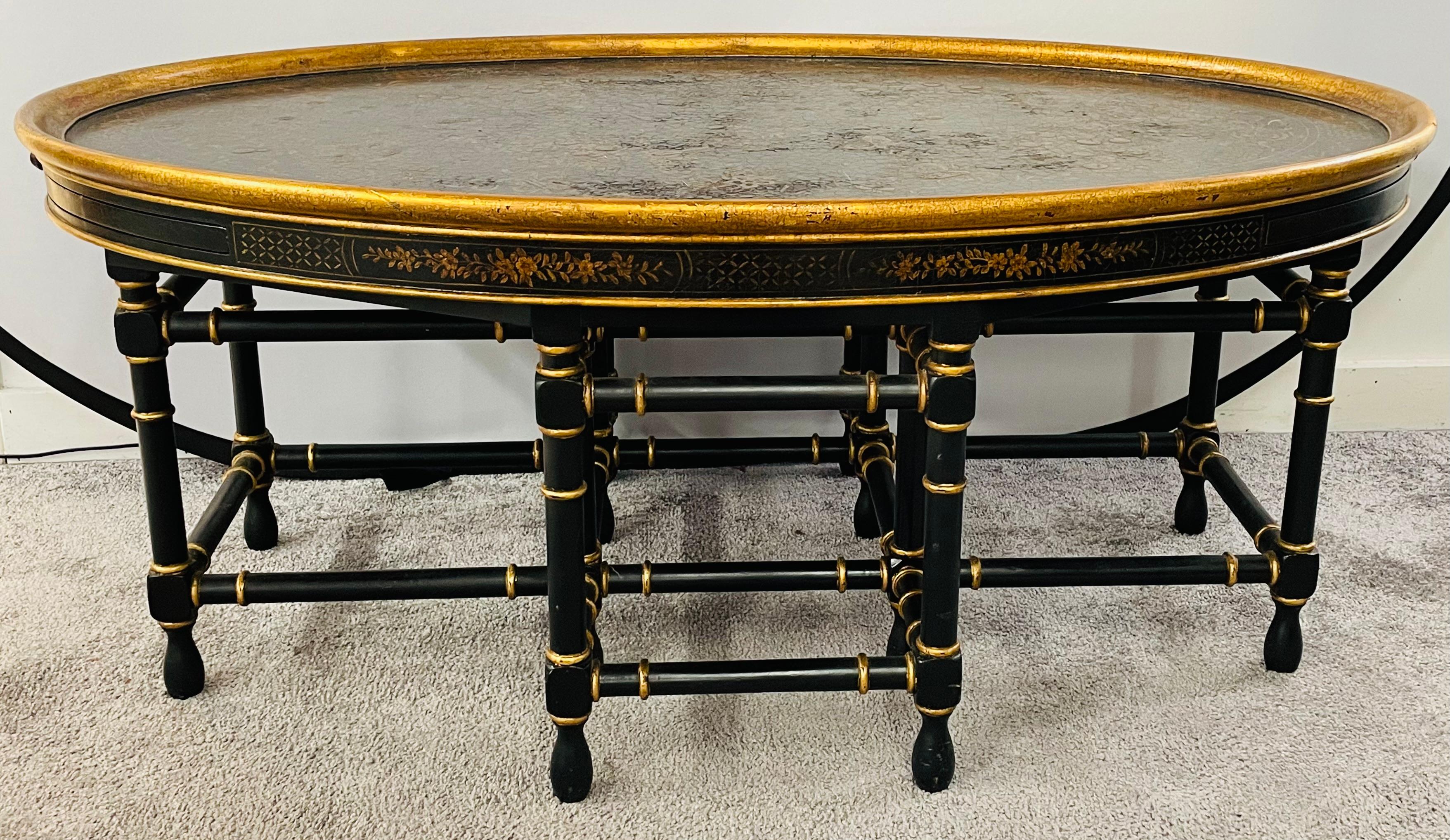 A versatile English Regency Chinoiserie style oval coffee table in black ebony and gold design. The table features intricate hand painted floral design and has two brown leather tooled pull out extensions from each side. The table is raised on faux