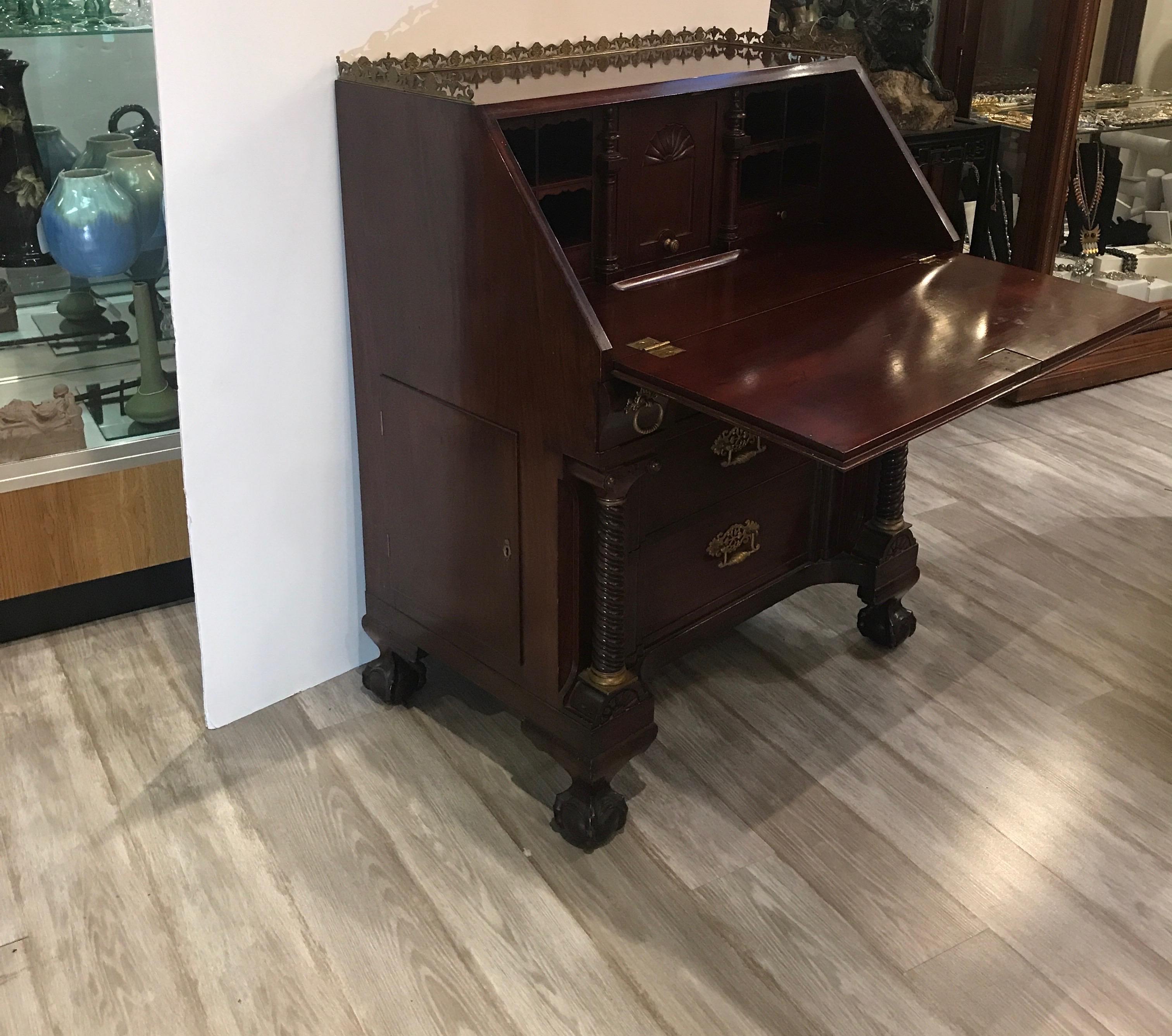 A hand carved Honduran mahogany slant top desk with original finish and hardware, circa 1870. The desk with multiple drawers and some hidden drawers and 2 safe sides. The ball and claw feet with original hidden castors.