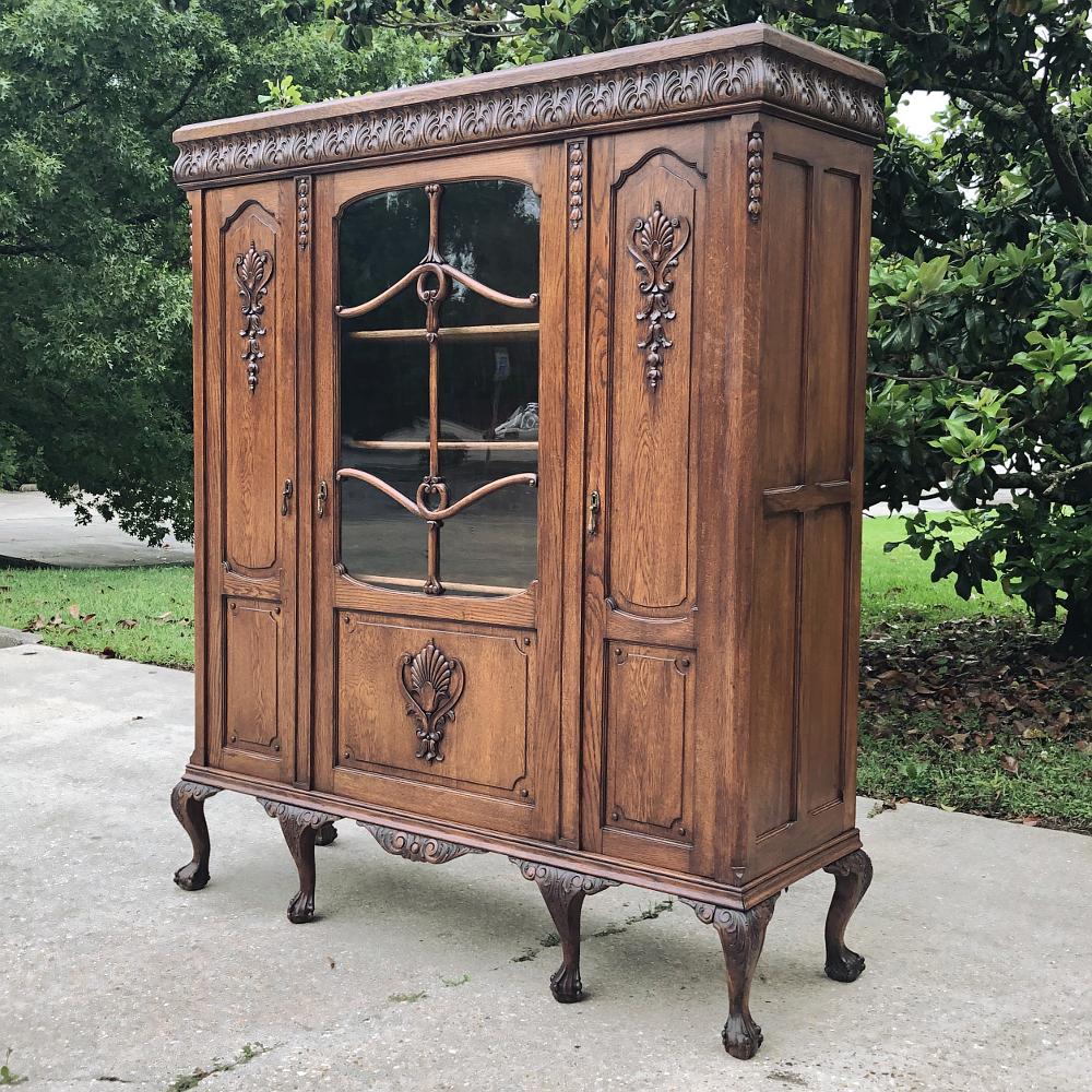 Antique English Chippendale triple oak bookcase is a classic, indeed! The bold foliate crown wraps around the entire facade, and overlooks the three doors below. The left and right doors are adorned with stylized shell and foliate motifs in relief,