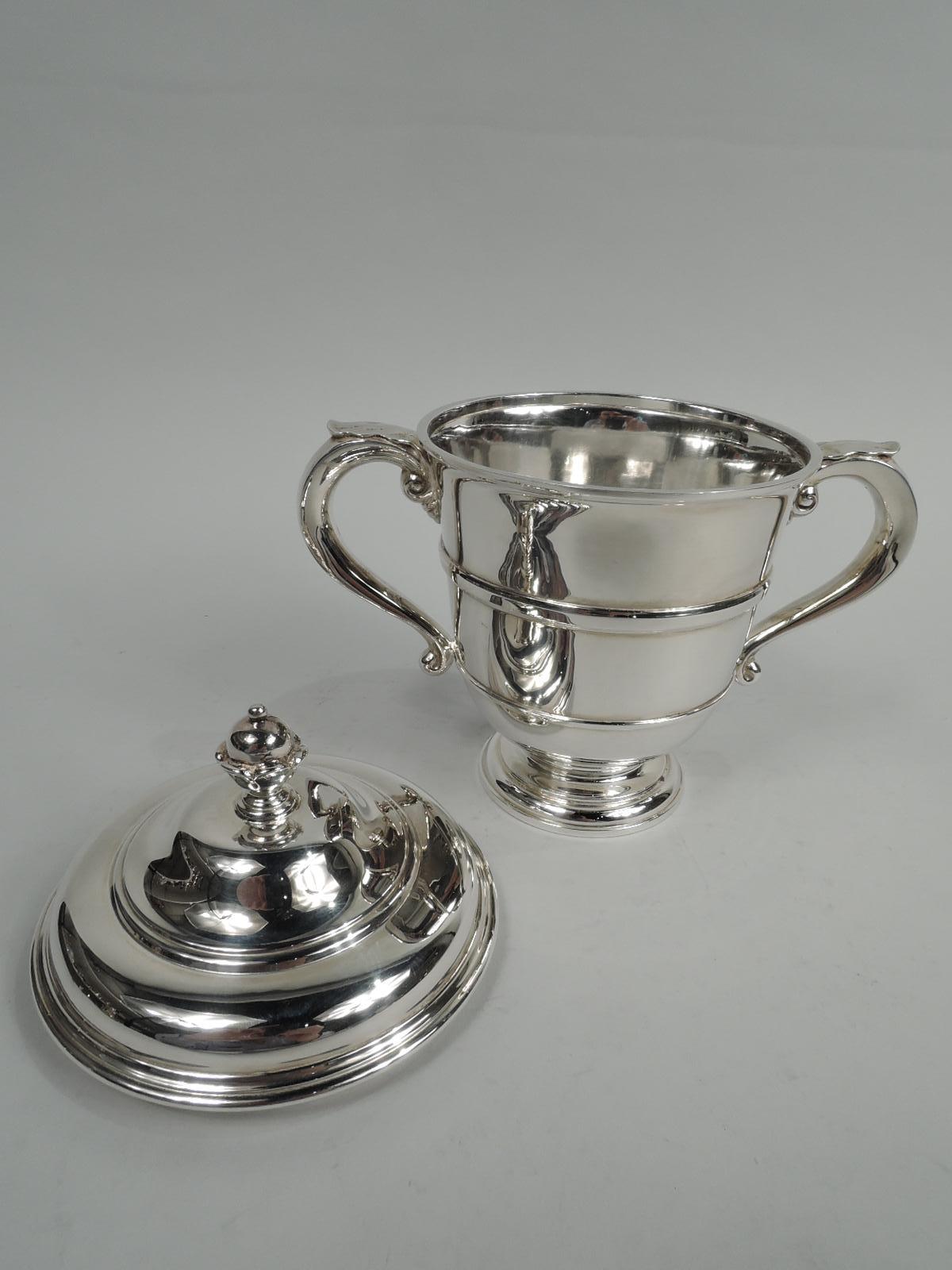 George V sterling silver trophy cup. Made by Charles & Richard Comyns in London in 1923. Girdled urn, round and stepped foot, and leaf-capped scroll handles. Cover double domed with bud finial. The classic winning form in small scale. Fully marked.