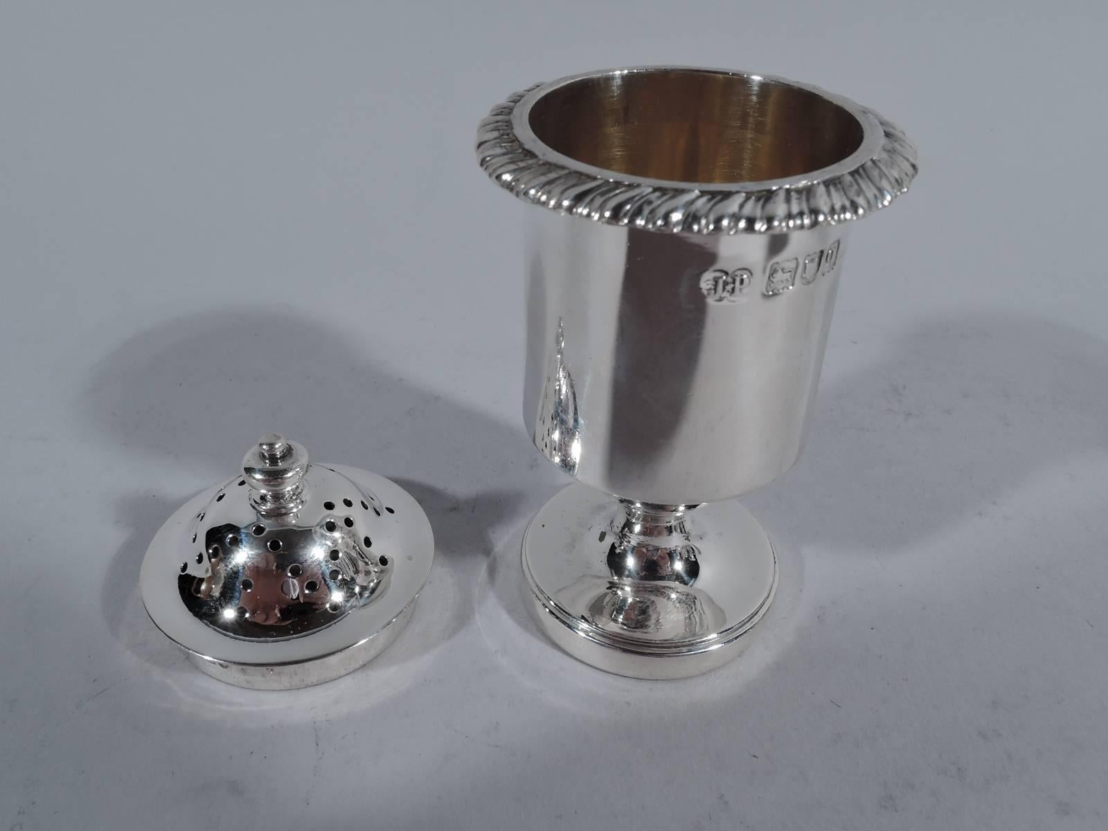 George V sterling silver pepper pot. Made by J. Parkes in London in 1911. Drum body, gadrooned flange, domed cover with pierced star and vase finial, and raised stepped foot. Interior has soft gilt wash. Hallmarked. Weight: 2.6 troy ounces.