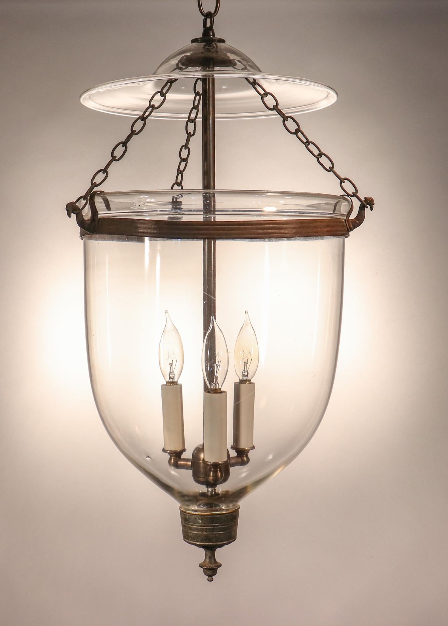 An antique bell jar lantern from England, circa 1860, with very good quality hand blown glass and particularly lovely form. The bell jar pendant features its original rolled brass band that is joined, brass finial/candleholder base, and chains. It